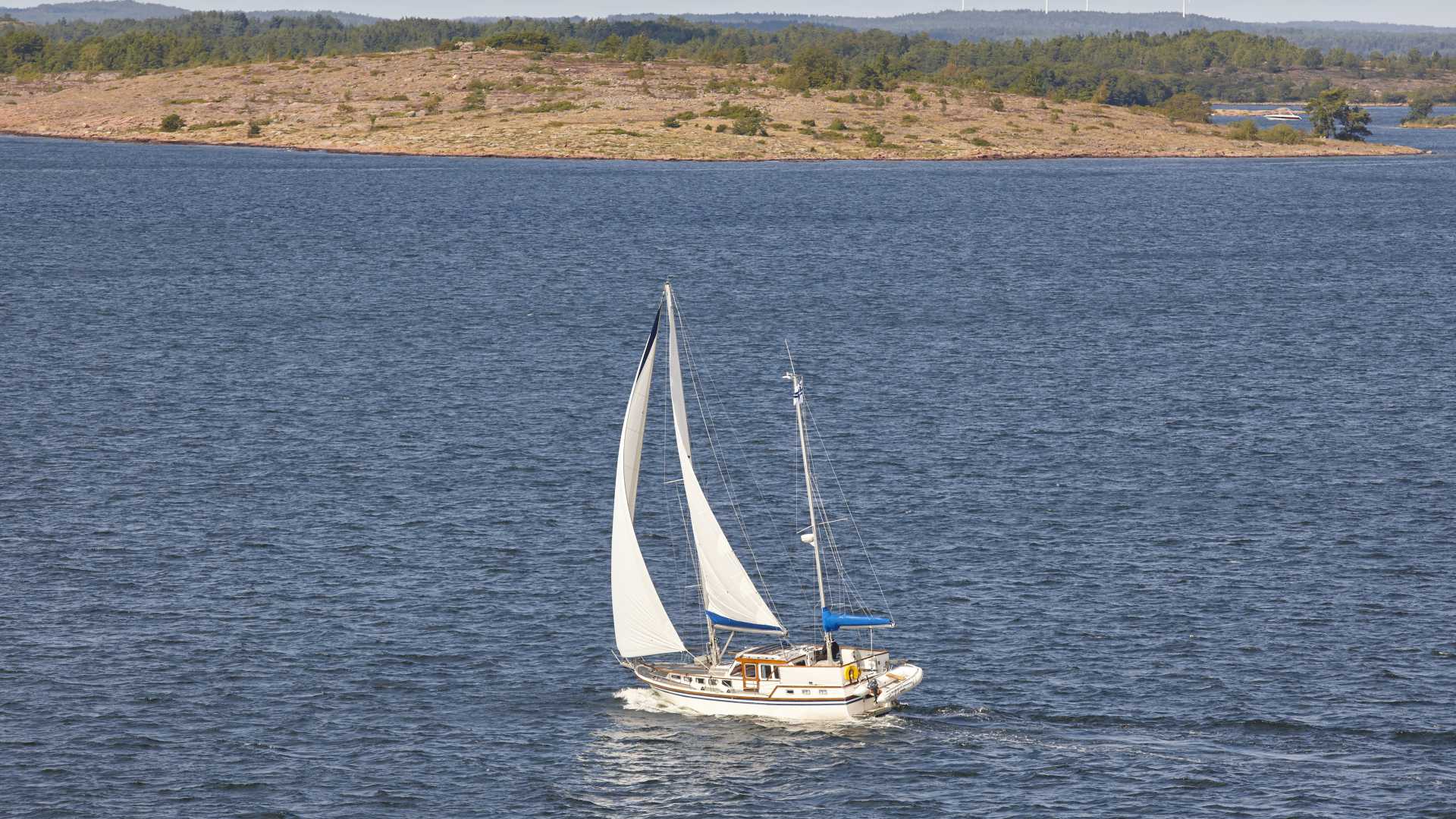 Een zeilboot glijdt door het blauwe water van de Åland-archipel, met een rustig eiland op de achtergrond.