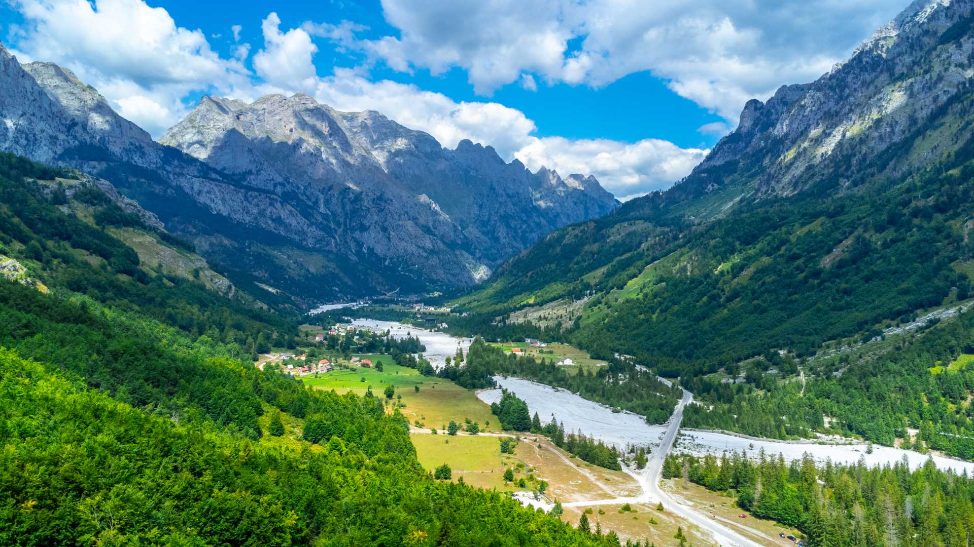 Luchtfoto van de Valbona-vallei, omgeven door weelderige groene bossen en torenhoge pieken in de Albanese Alpen.