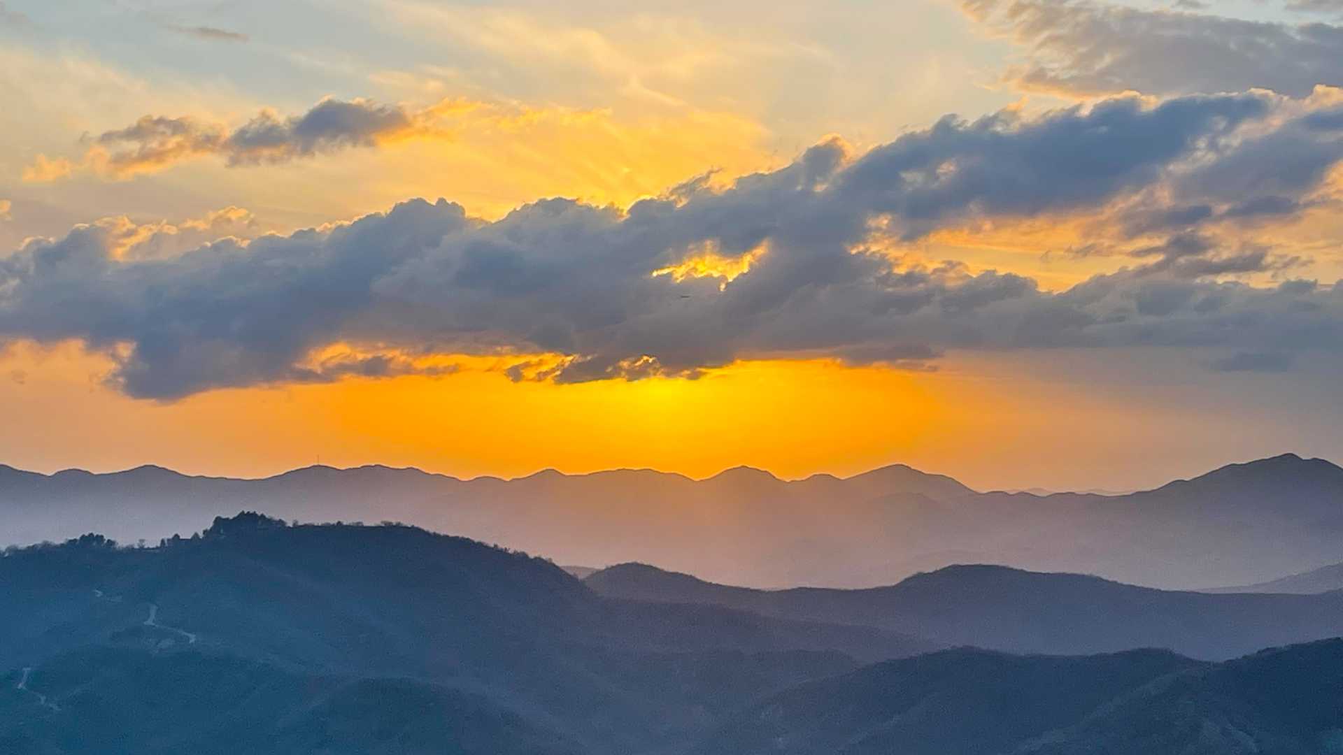 A vivid sunset illuminates the rolling Albanian mountains with a spectrum of orange and yellow colors.