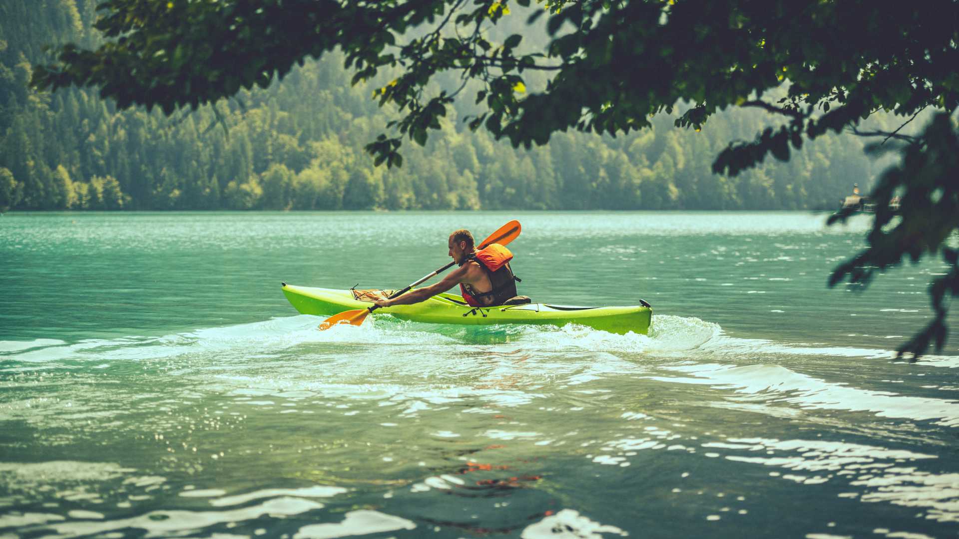Een kajakker peddelt door het turquoise water van de Weissensee, omgeven door weelderig bos in Karinthië, Oostenrijk.