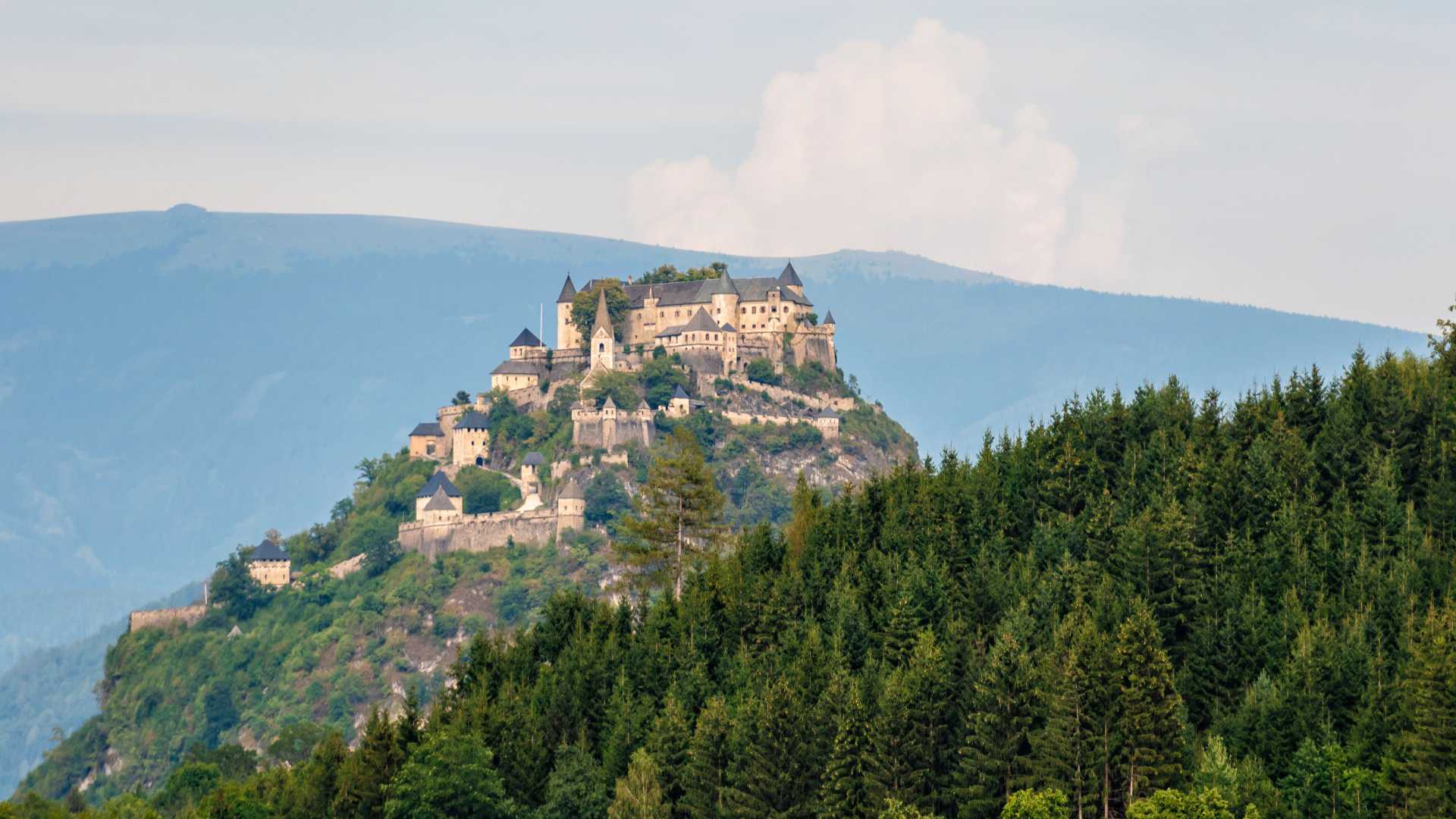 Kasteel Hochosterwitz domineert trots een weelderige heuveltop, omgeven door een dicht bos en een achtergrond van mistige bergen in Karinthië, Oostenrijk.