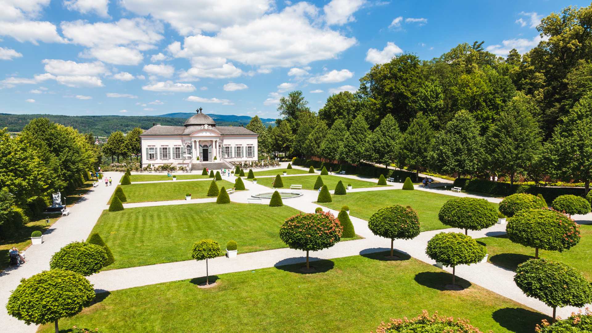 Elegant onderhouden tuinen met een historisch paviljoen in Abdij Melk, omlijst door weelderige bomen en een heldere lucht.