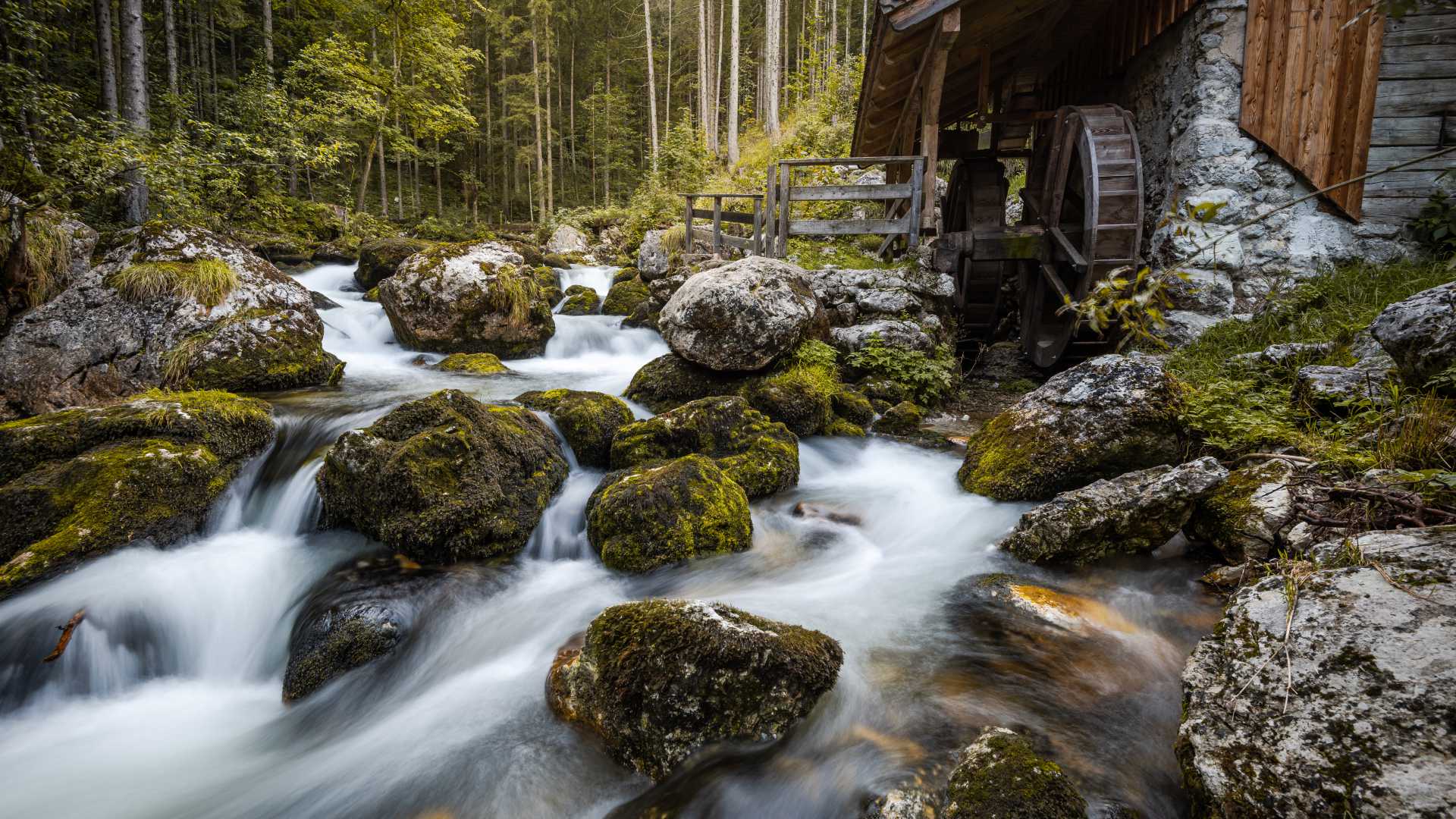Een rustieke houten watermolen bij een beek, omgeven door een weelderig bos in de buurt van de Golling-waterval, Oostenrijk.