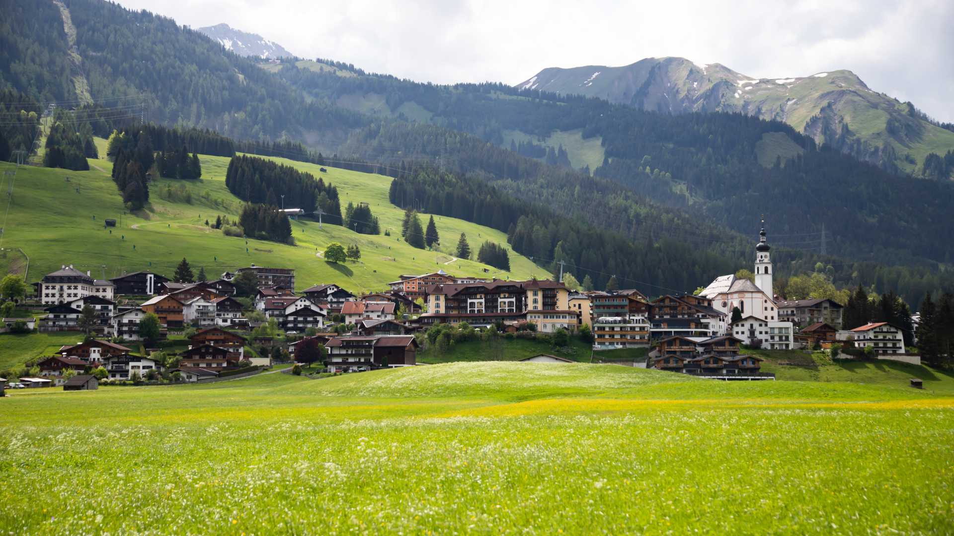 Lermoos, Oostenrijk: Alpendorp met traditionele huizen, kerk, weiden en bergen op de achtergrond in de lente.