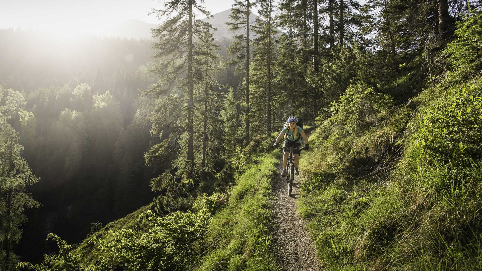 Een vrouw die geniet van een mountainbiketocht over een zonovergoten bospad in Lermoos, Tirol, Oostenrijk.