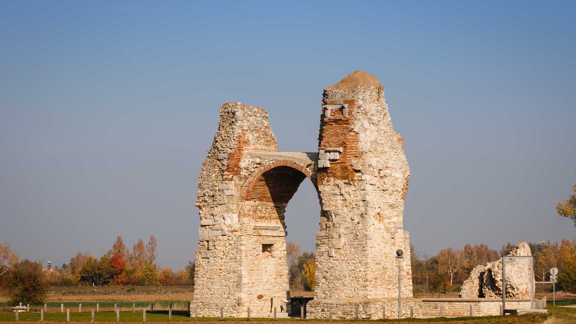 De oude Romeinse poort bij Carnuntum, Oostenrijk, onder een helderblauwe hemel met herfstbomen op de achtergrond.