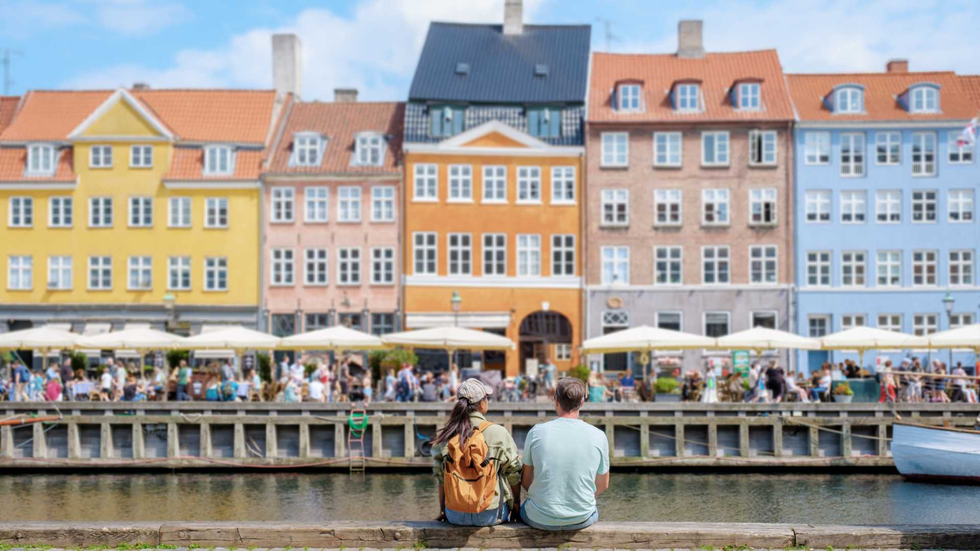 Un couple se détend au bord du canal de Nyhavn à Copenhague, admirant les bâtiments colorés du front de mer et l'atmosphère animée.