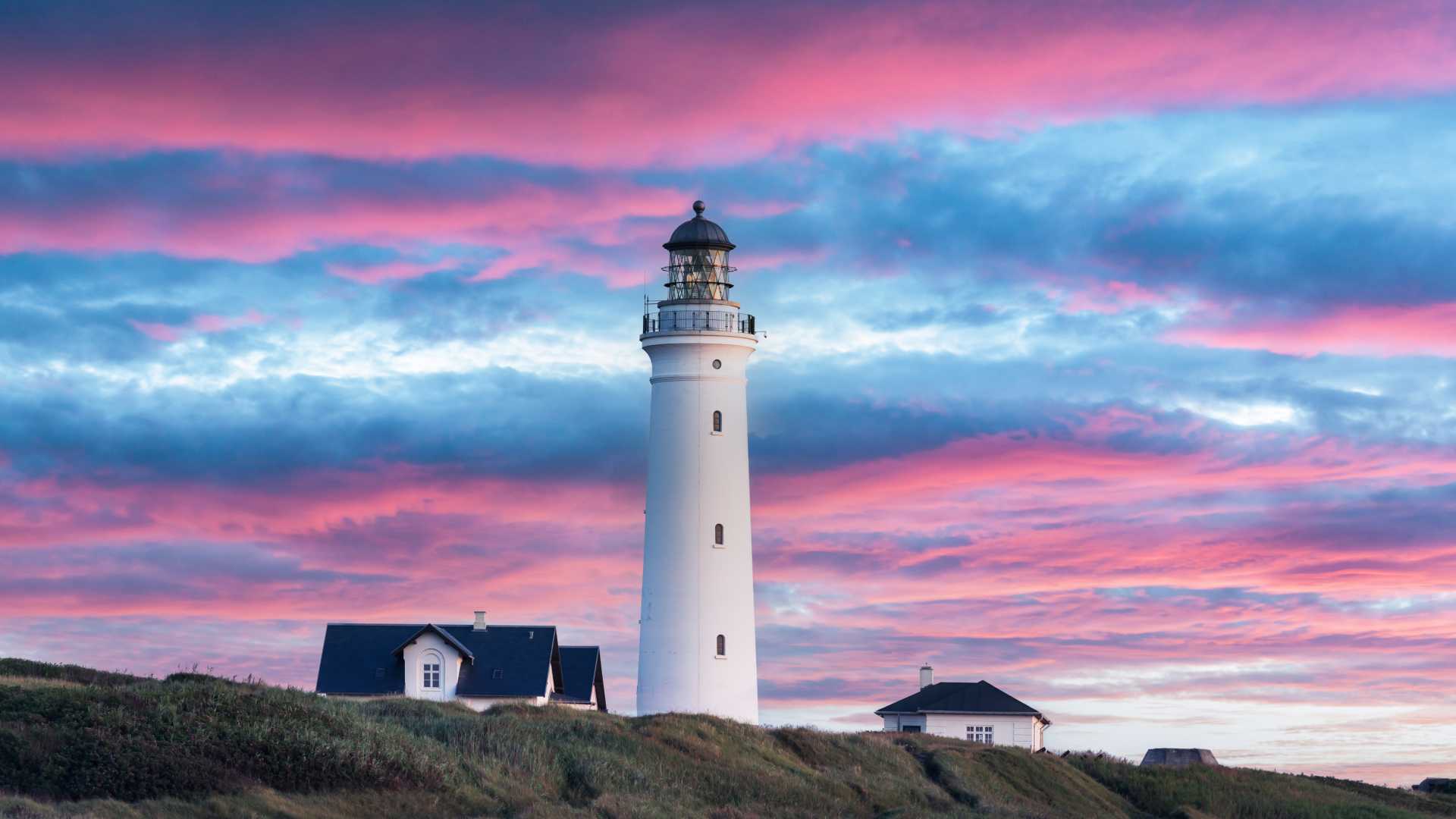덴마크 히르츠할스에서 눈에 띄는 분홍색과 파란색 일몰 하늘을 배경으로 실루엣으로 보이는 흰색 등대.