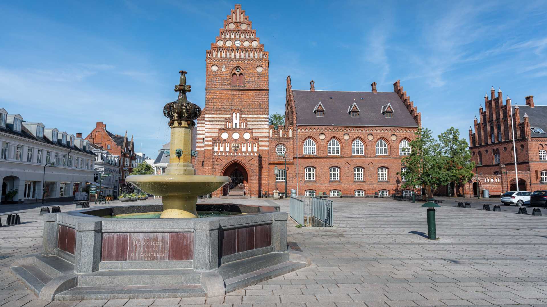 맑고 푸른 하늘 아래 붉은 벽돌 외관과 클래식한 분수가 있는 로스킬데 시청 광장.