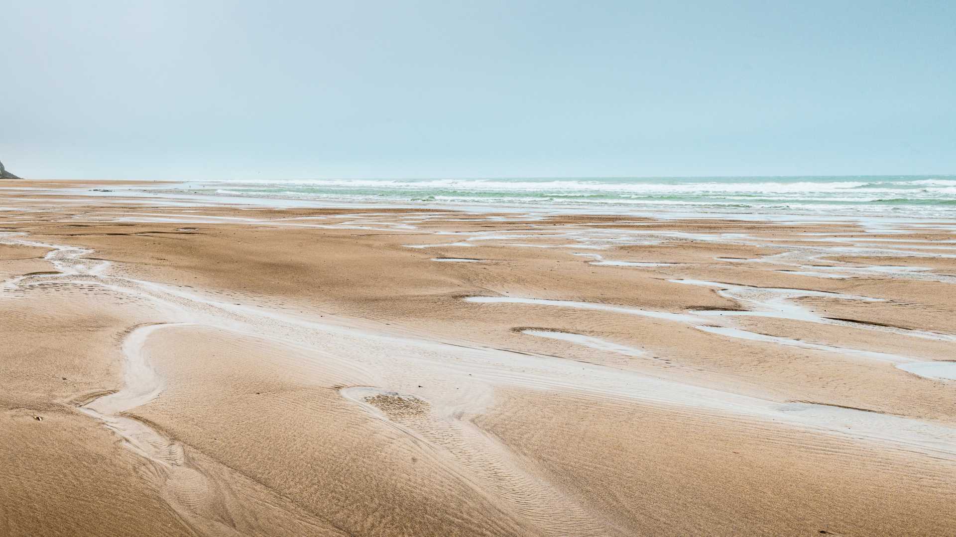 Expansive sandy beach at Cap Blanc-Nez with gentle waves and a distant chalk cliff under a pale sky.