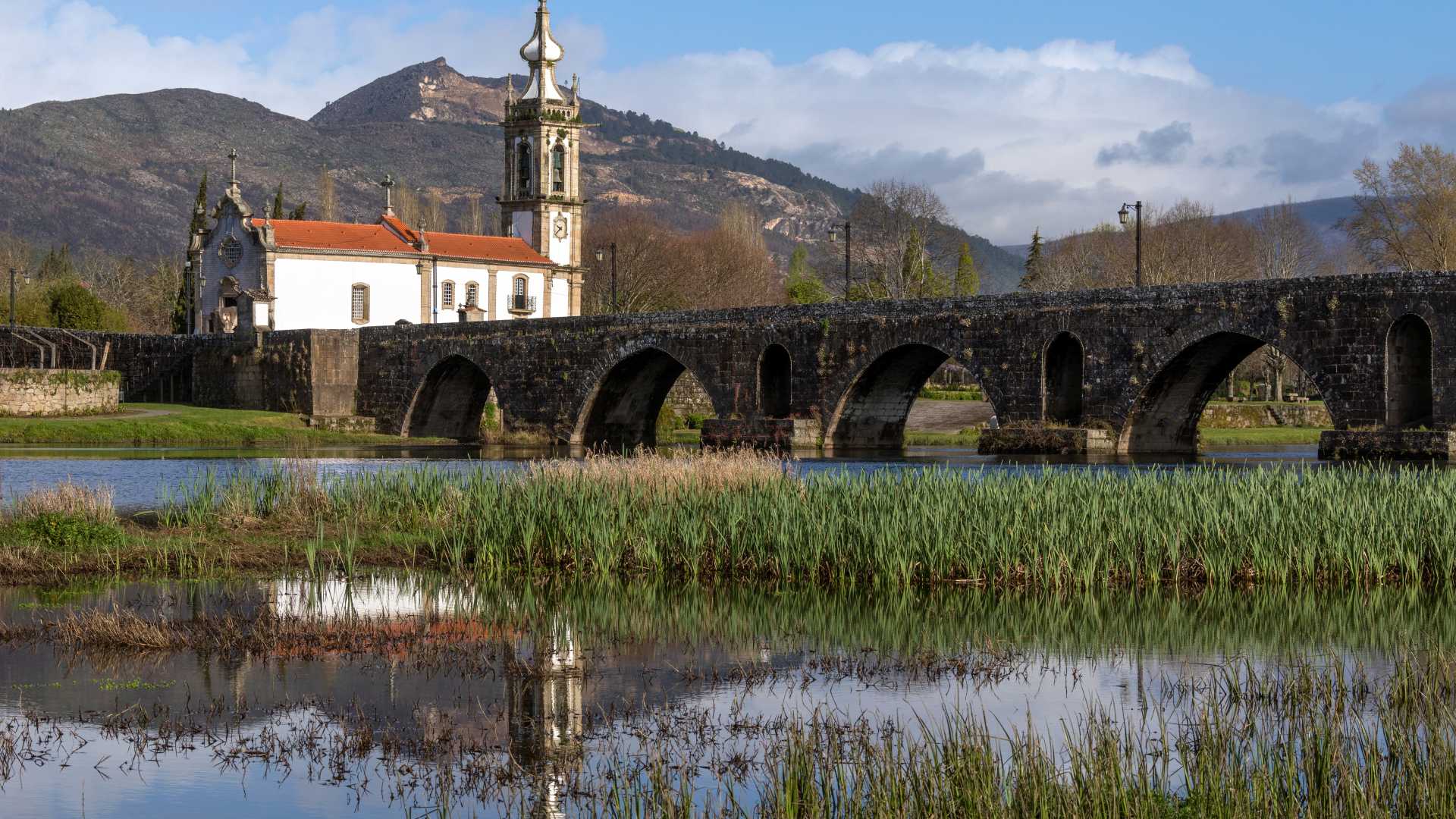 Ponte medievale in pietra sul fiume Limia con una chiesa bianca e montagne sullo sfondo a Ponte de Lima, Portogallo.