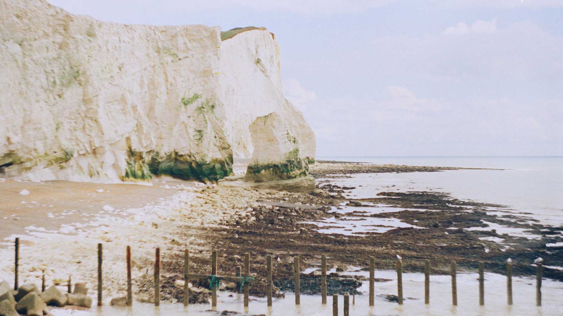 Witte krijtrotsen en rotsstrand bij Seaford, Sussex, met een kalme zee onder een bewolkte lucht.