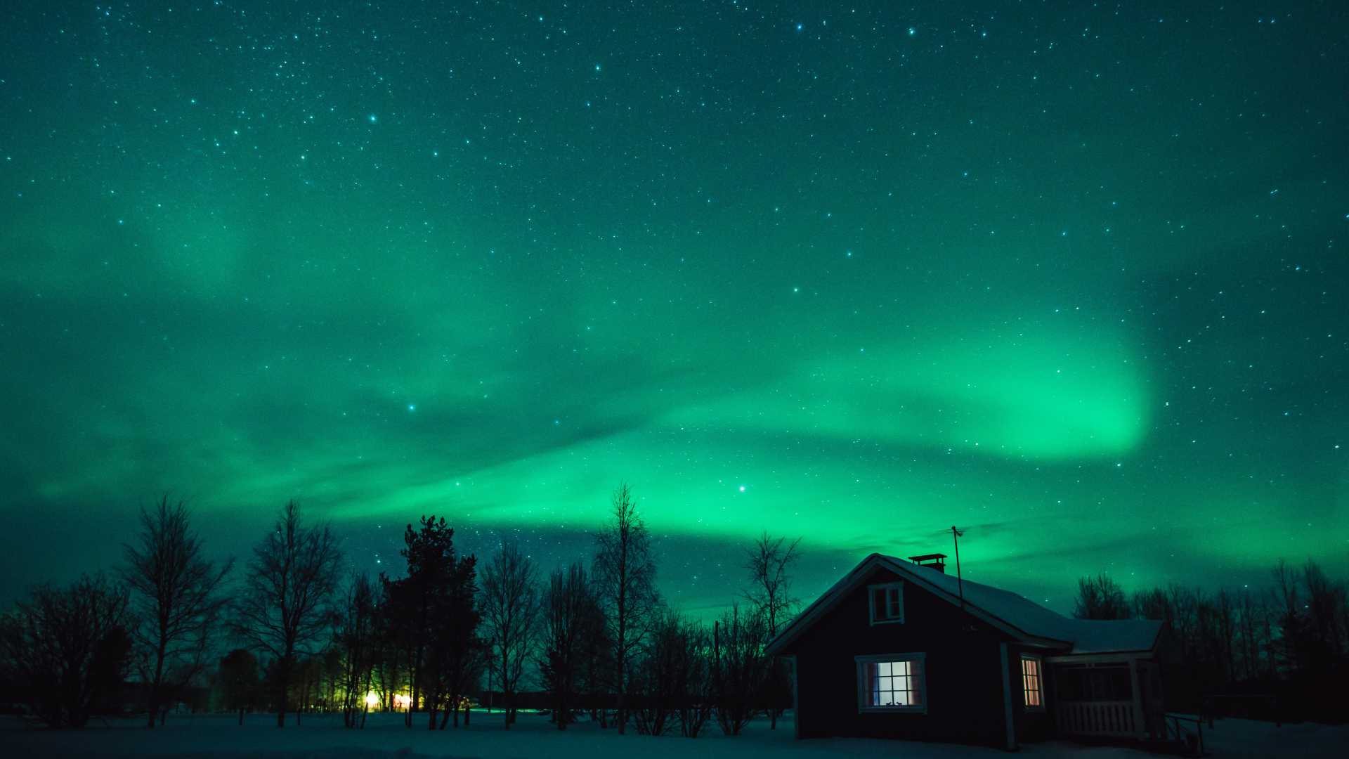 The northern lights illuminate the night sky above a snow-covered cottage in a peaceful Lapland village, Finland.
