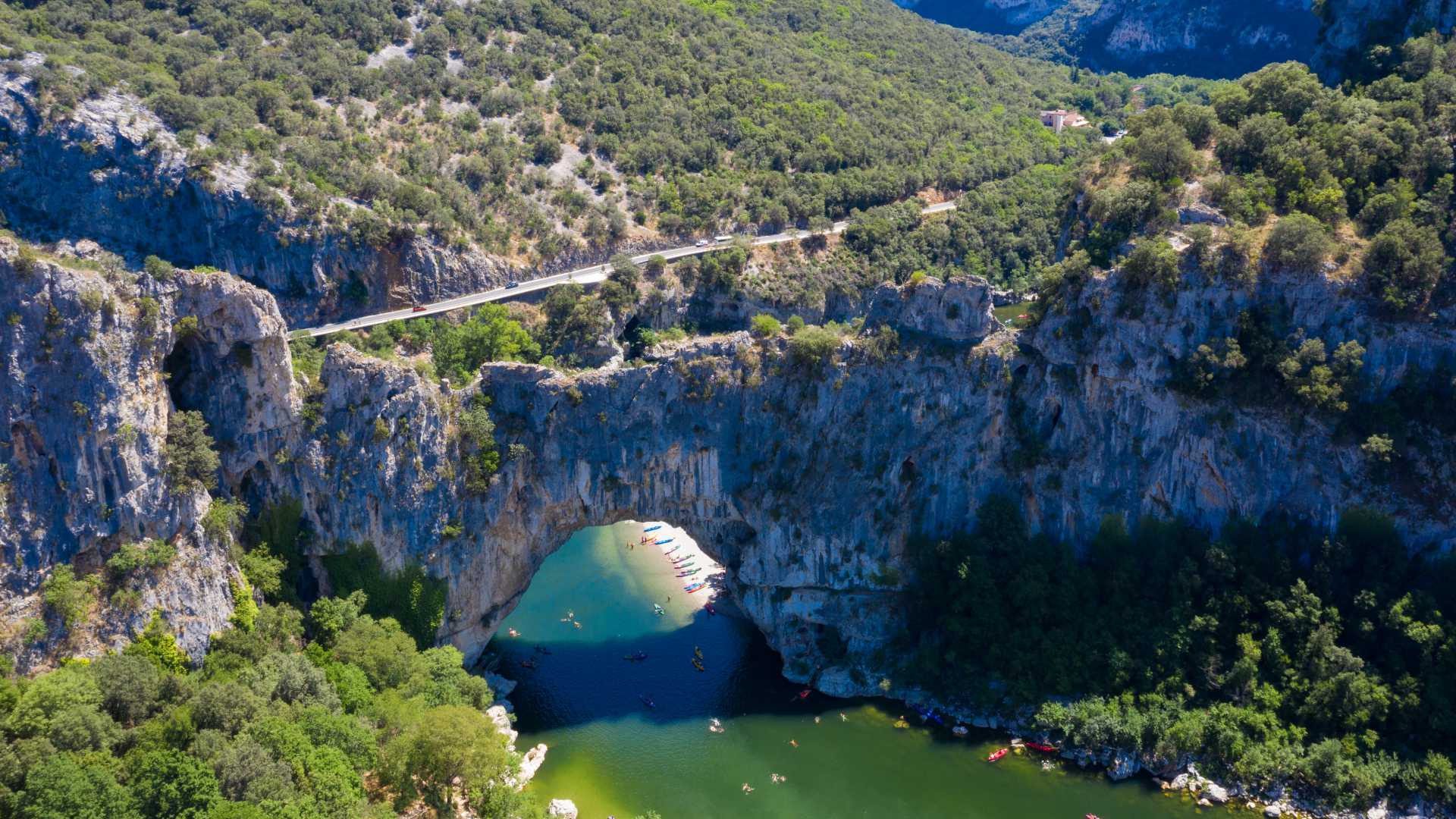 Vista aerea dell'arco di pietra naturale a Vallon-Pont-d'Arc in Ardèche, Francia, con kayakisti che esplorano il fiume sottostante.