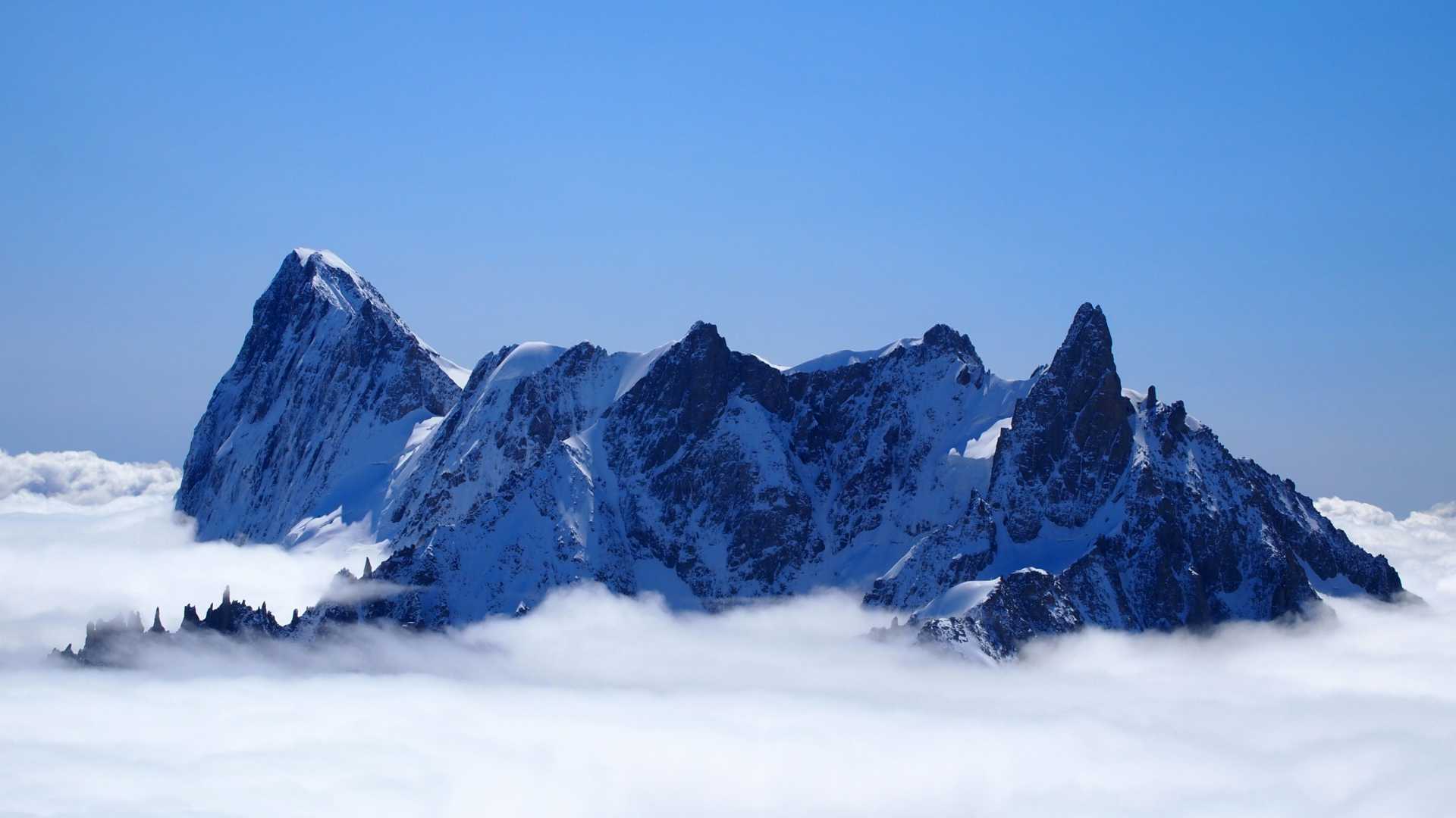 Sneeuwbedekte toppen van Chamonix die oprijzen uit een wolkenzee onder een helderblauwe lucht.