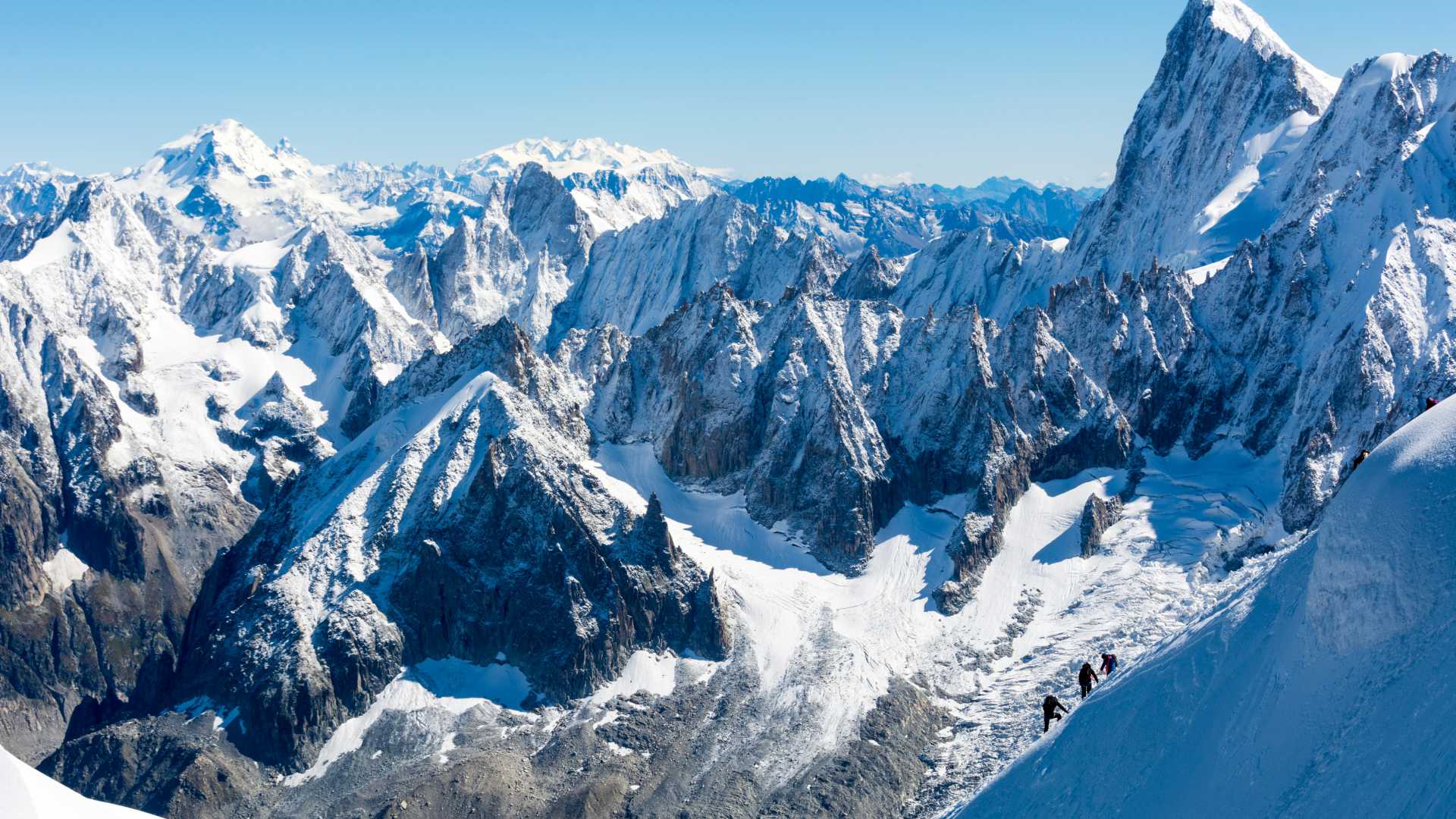 Les sommets enneigés du Chamonix-Mont-Blanc avec des alpinistes en pleine ascension, sur fond de ciel bleu.