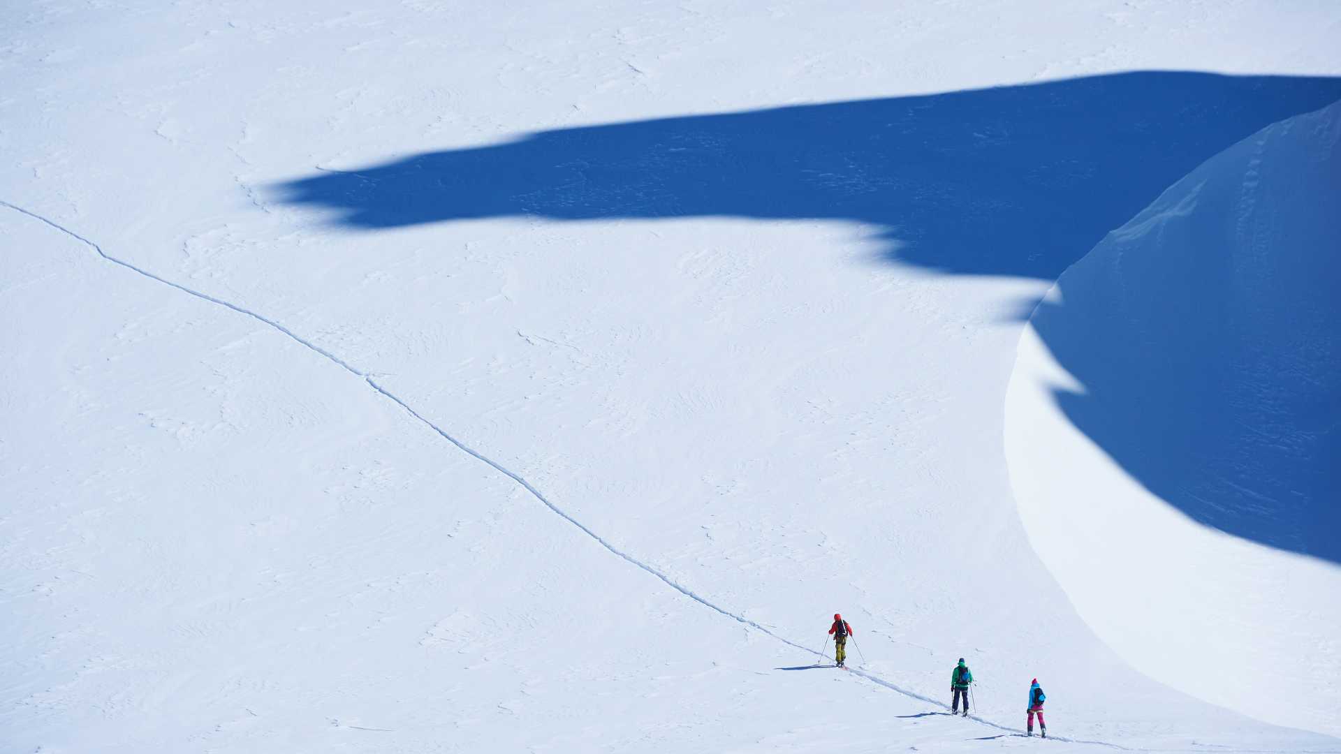 Drie skiërs doorkruisen een besneeuwde piste onder een uitgestrekte schaduw op het Mont Blanc massief, Grajische Alpen, Frankrijk.