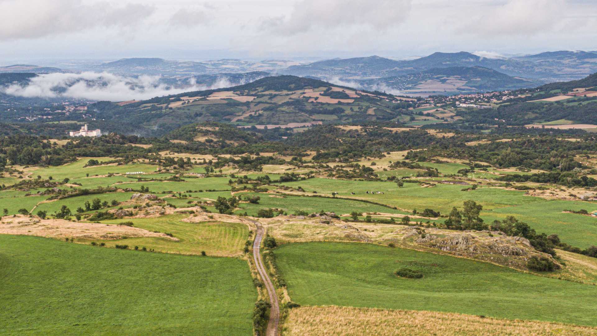 Weelderige groene velden en zachte heuvels omringen Olloix, met mistige bergen aan de horizon.