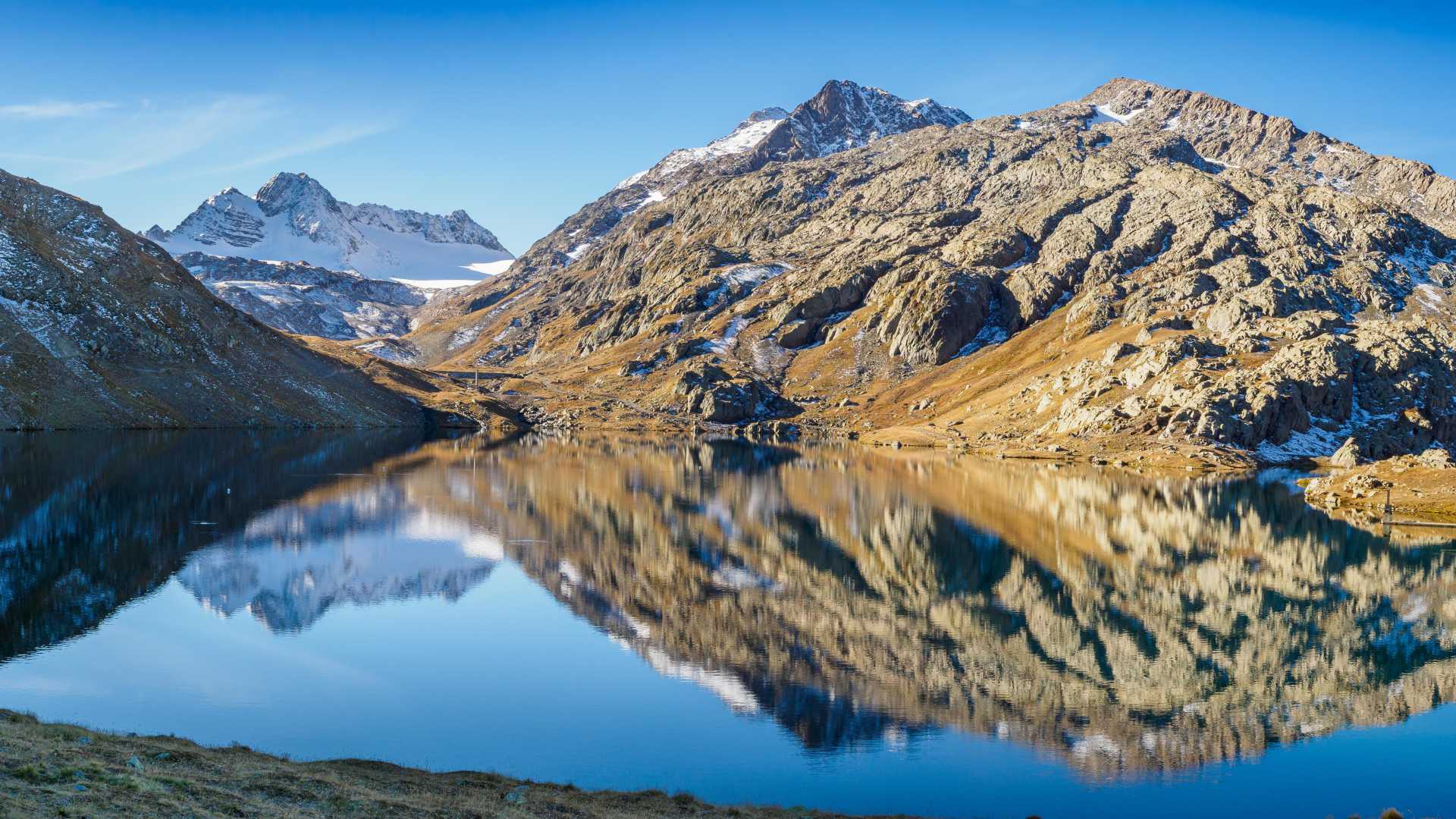 Las aguas cristalinas del lago Bramant reflejan las imponentes montañas y el glaciar de St Sorlin bajo un cielo azul claro.