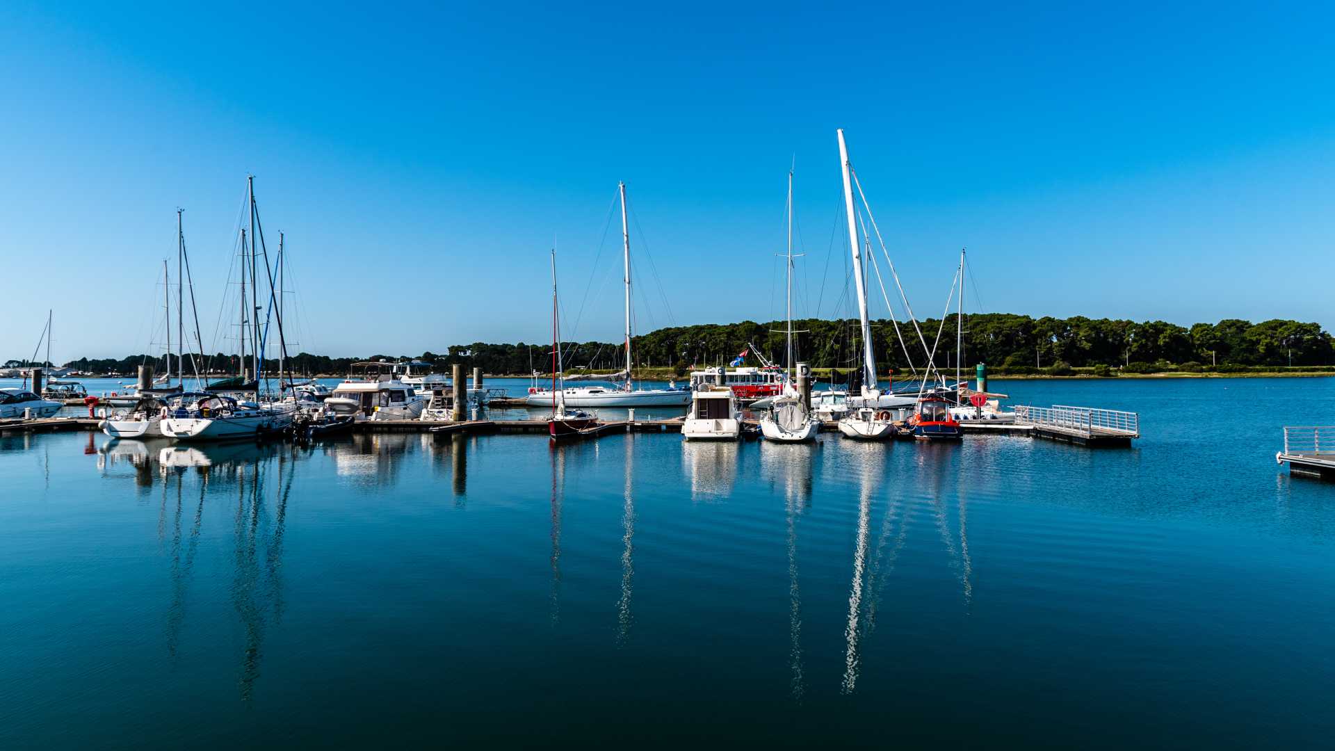 Zeilboten en jachten aangemeerd in de serene Keroman-jachthaven in Lorient, onder een heldere blauwe lucht.