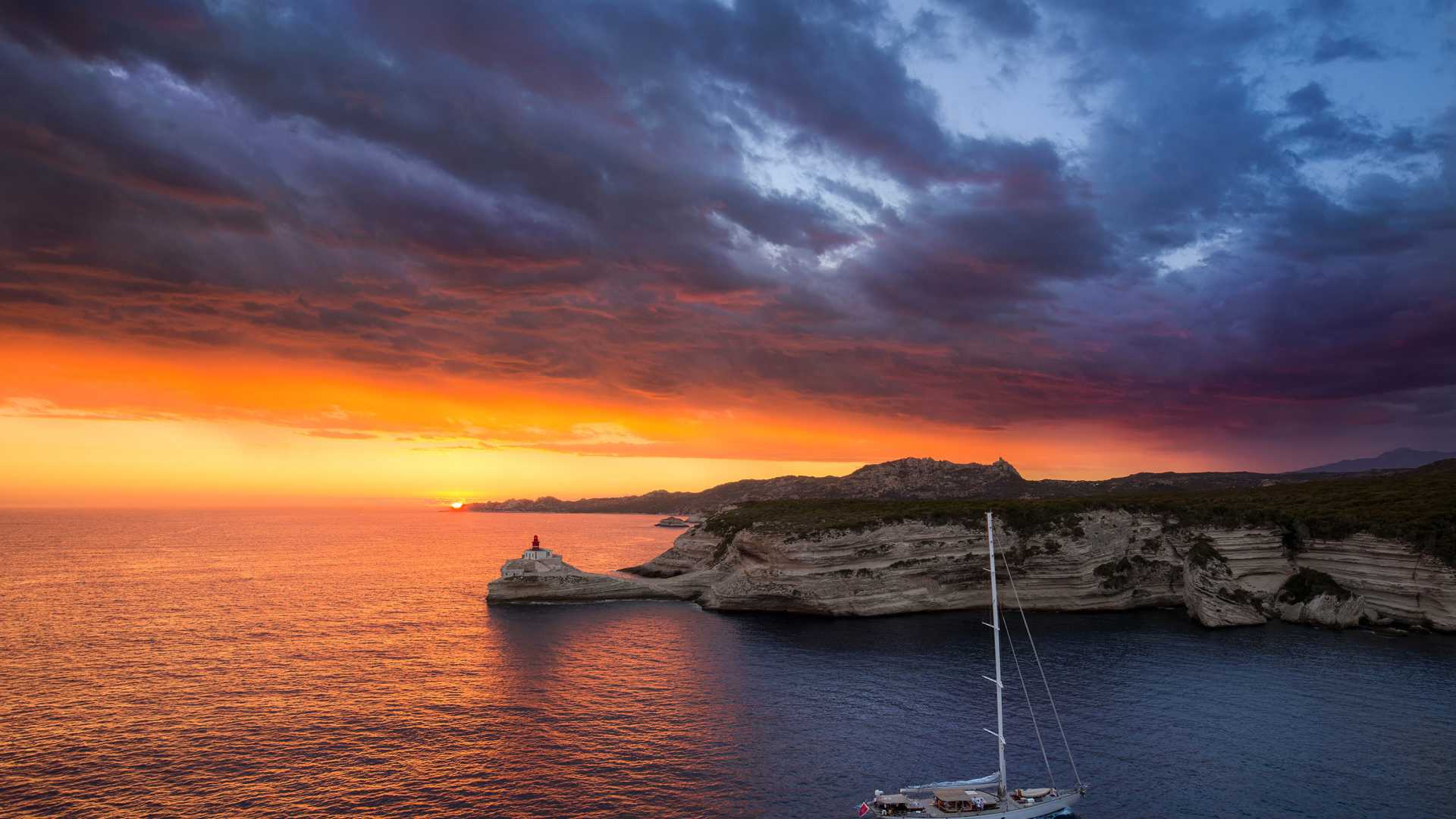 Fiery sunset over Bonifacio lighthouse, with dramatic cliffs and serene sea, Corsica, France.