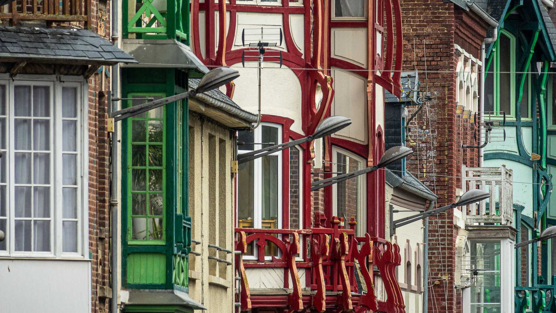 Fachadas coloridas y ornamentadas de casas en Mers-les-Bains, mostrando intrincados balcones de madera y tonos vivos.