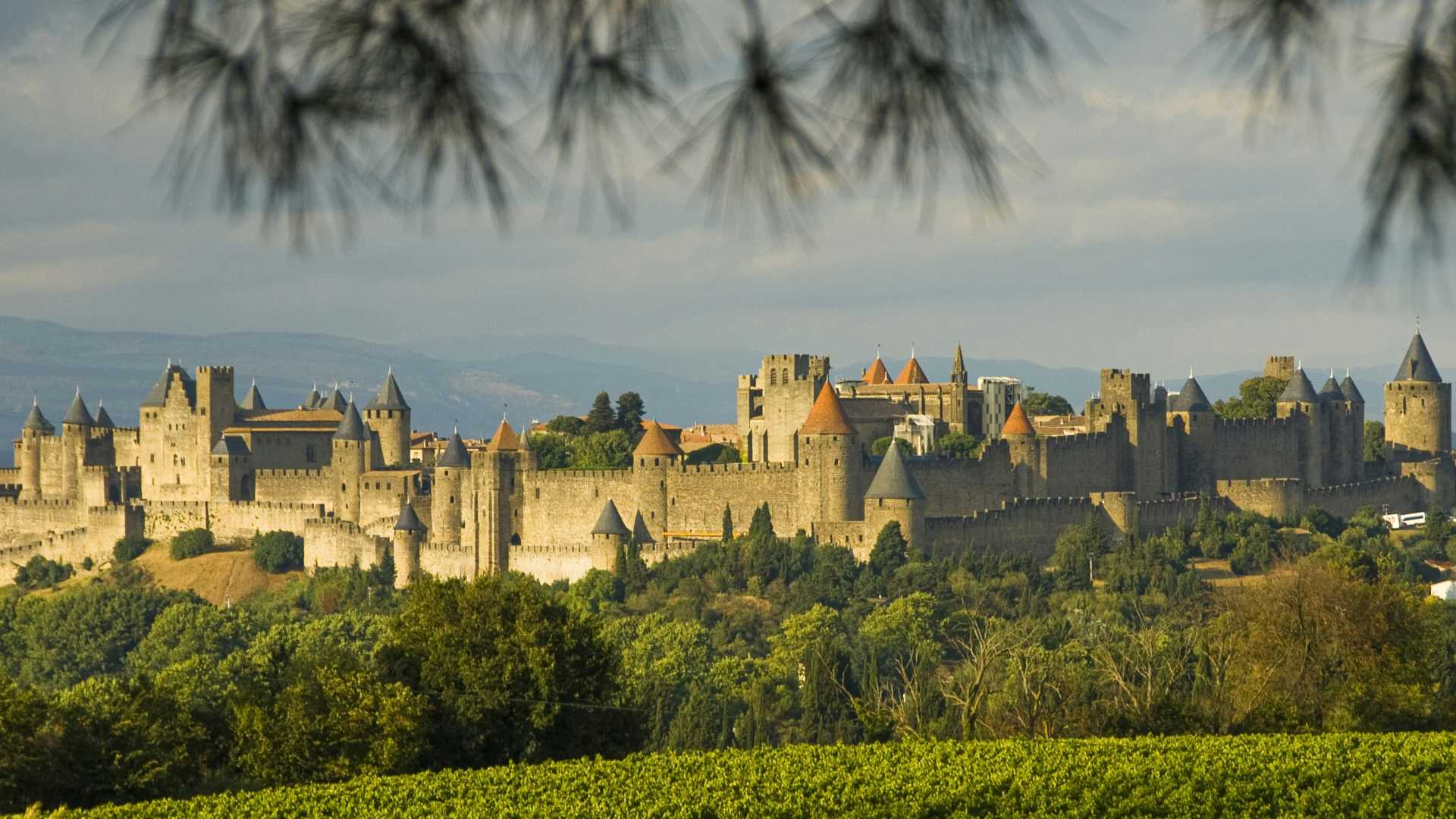 L'impressionnante forteresse médiévale de Carcassonne sous un ciel avec quelques nuages, entourée d'un paysage verdoyant dans la région de l'Aude, en France.