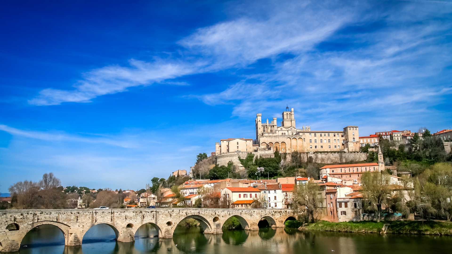 Paysage urbain de Béziers avec la cathédrale au sommet d'une colline et un pont de pierre historique sur l'Orb.