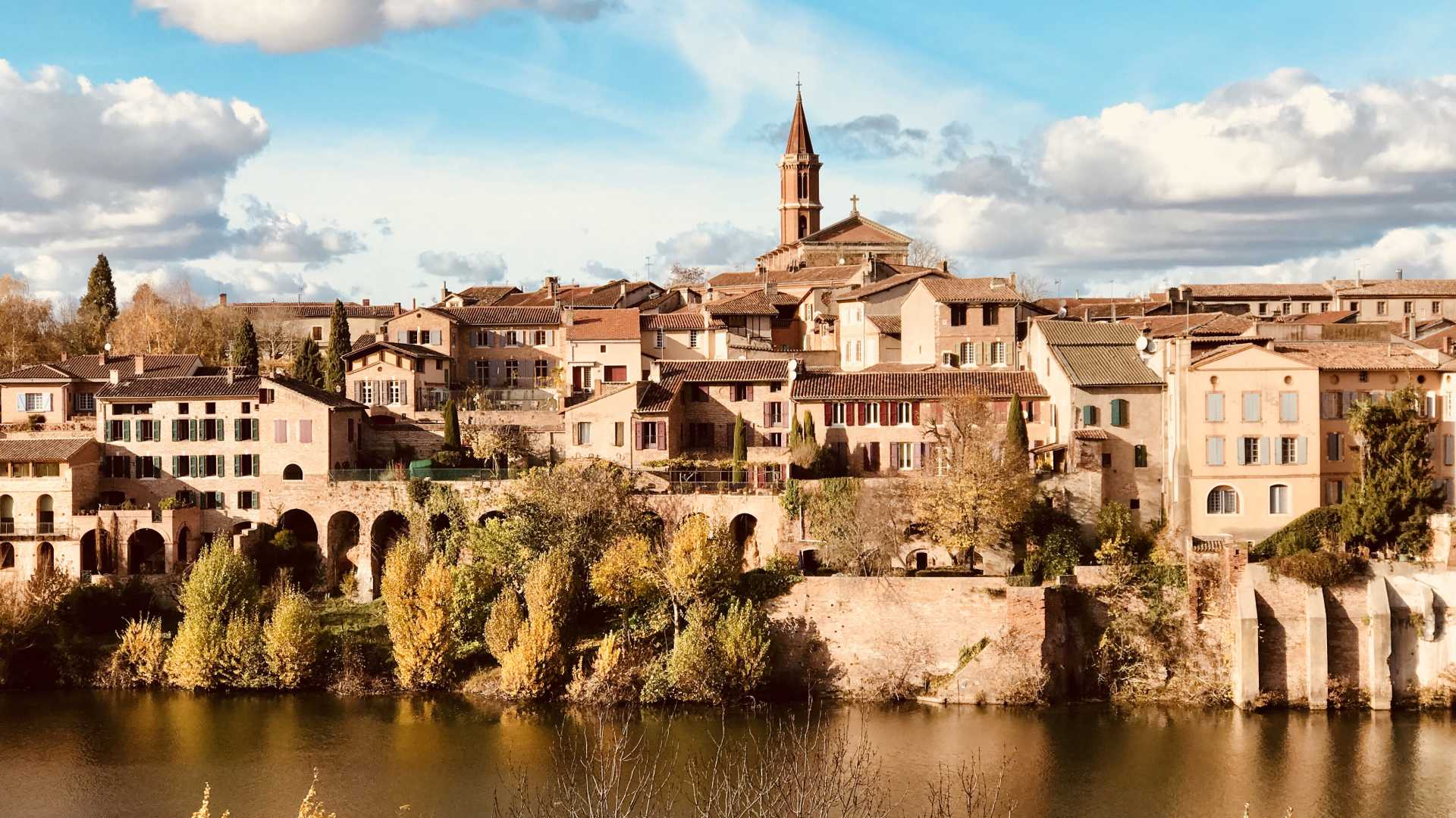 Vue charmante d'Albi avec ses bâtiments historiques, la cathédrale Sainte-Cécile et la rivière Tarn sous un ciel lumineux.