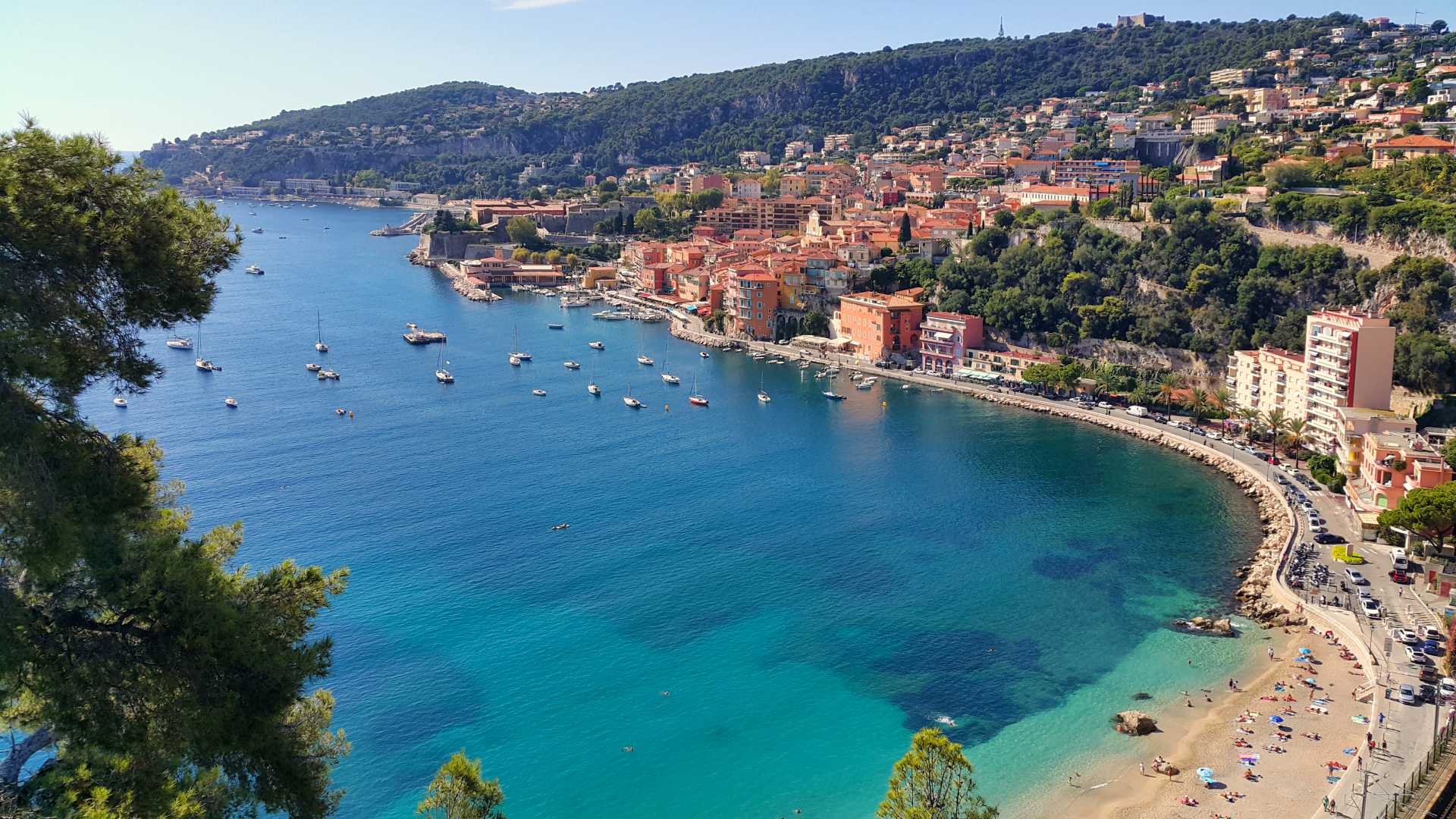 Des bâtiments colorés bordent le port de Villefranche-sur-Mer, avec des eaux turquoise et des collines verdoyantes le long de la Côte d'Azur.