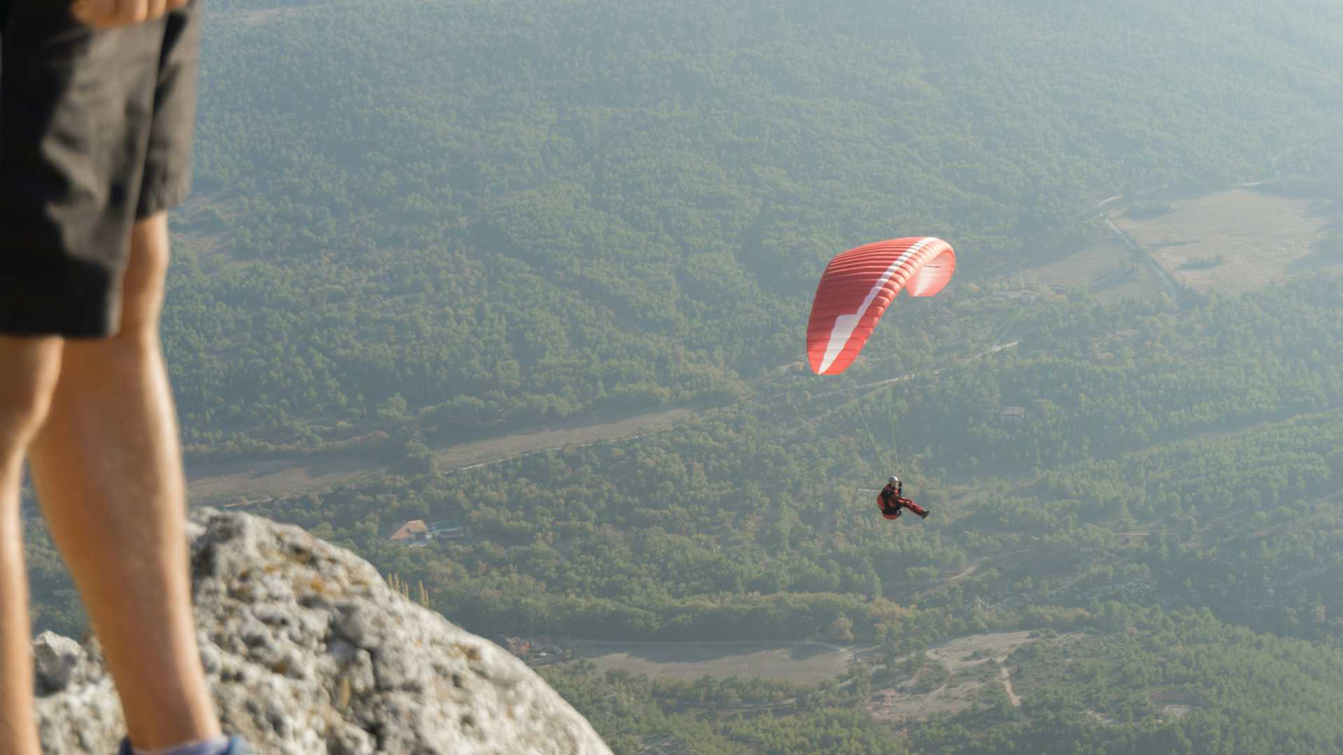Un parapentiste avec une voile rouge profite de vues panoramiques sur un paysage luxuriant et verdoyant en Provence.