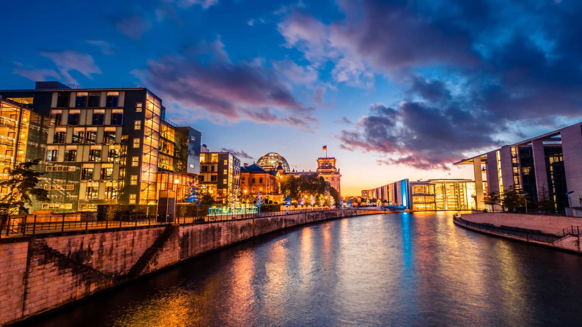 Berlin's evening skyline with the Reichstag Dome and river reflections under a vibrant sky.