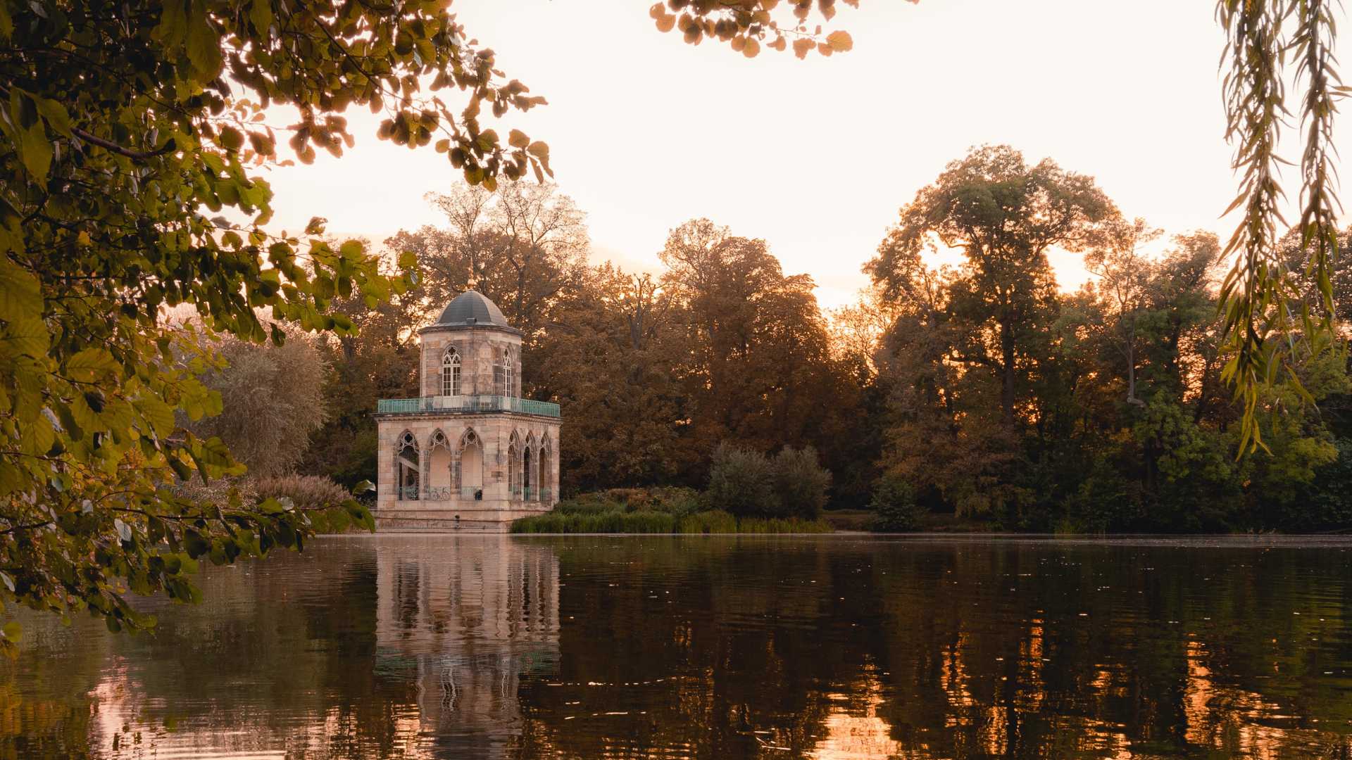 Gothic Library at Heiliger See in Potsdam, framed by autumn trees, reflecting in the tranquil lake.