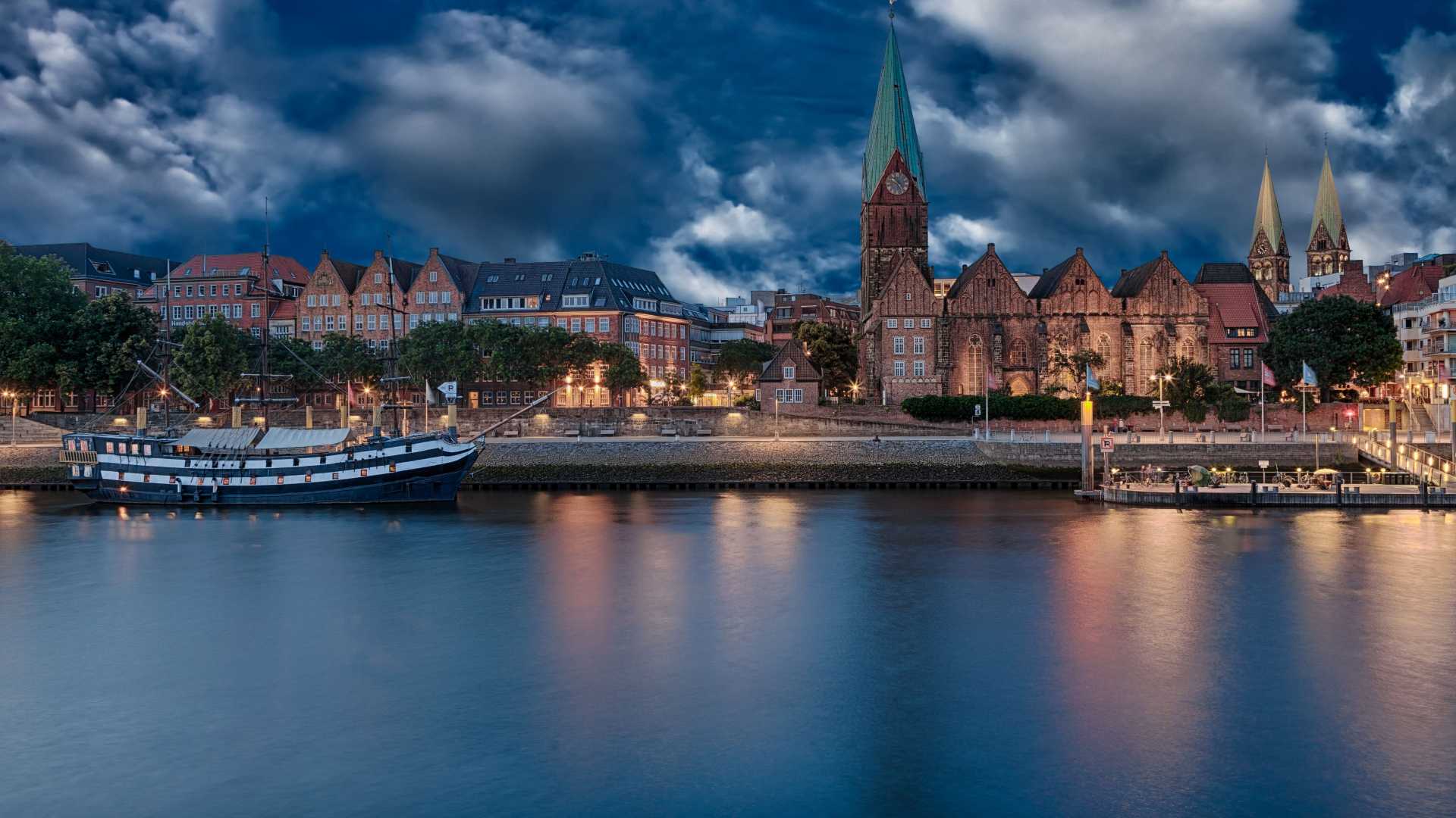 Evening view of Bremen's historic buildings along the Weser River, with a traditional ship adding to the city's charm.