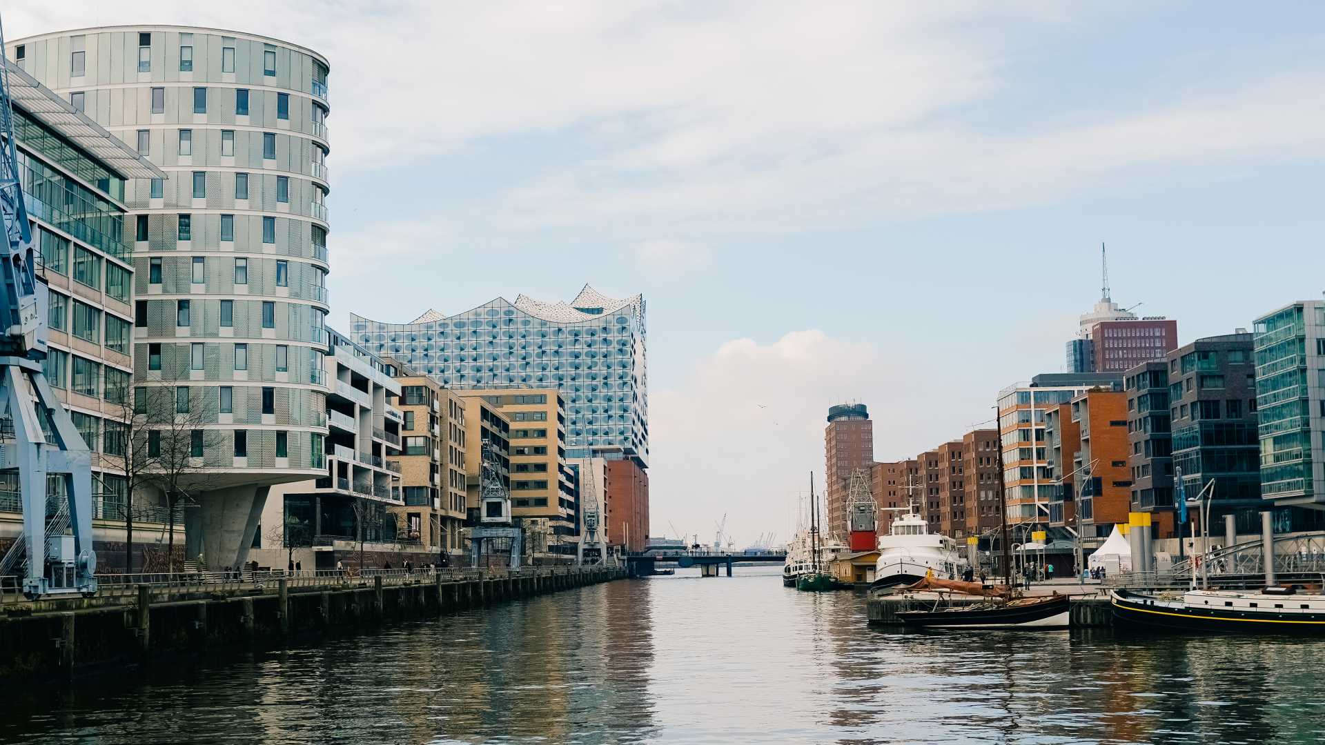 Modern buildings and boats line Sandtorhafen canal with the Elbphilharmonie in the background, Hamburg.
