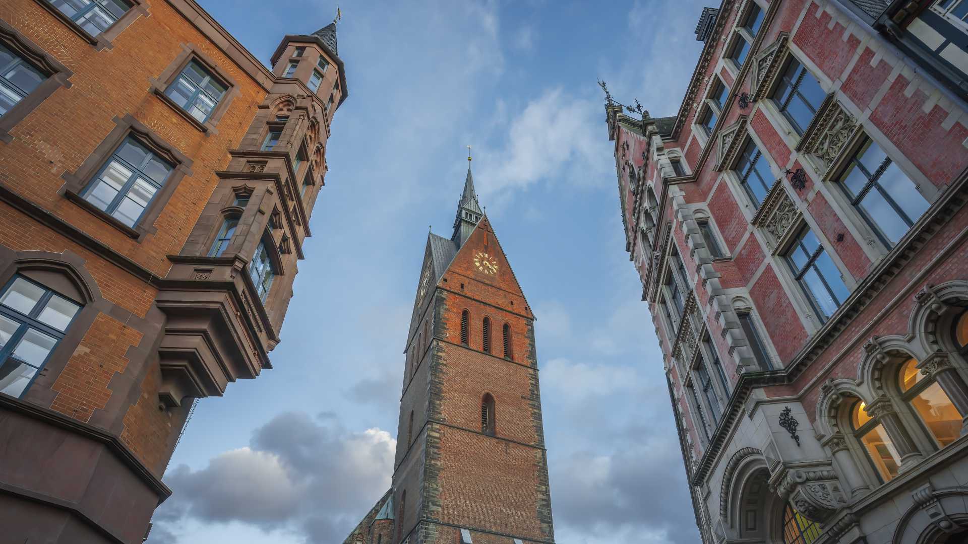 The towering Market Church (Marktkirche) in Hanover framed by historic buildings under a blue sky.