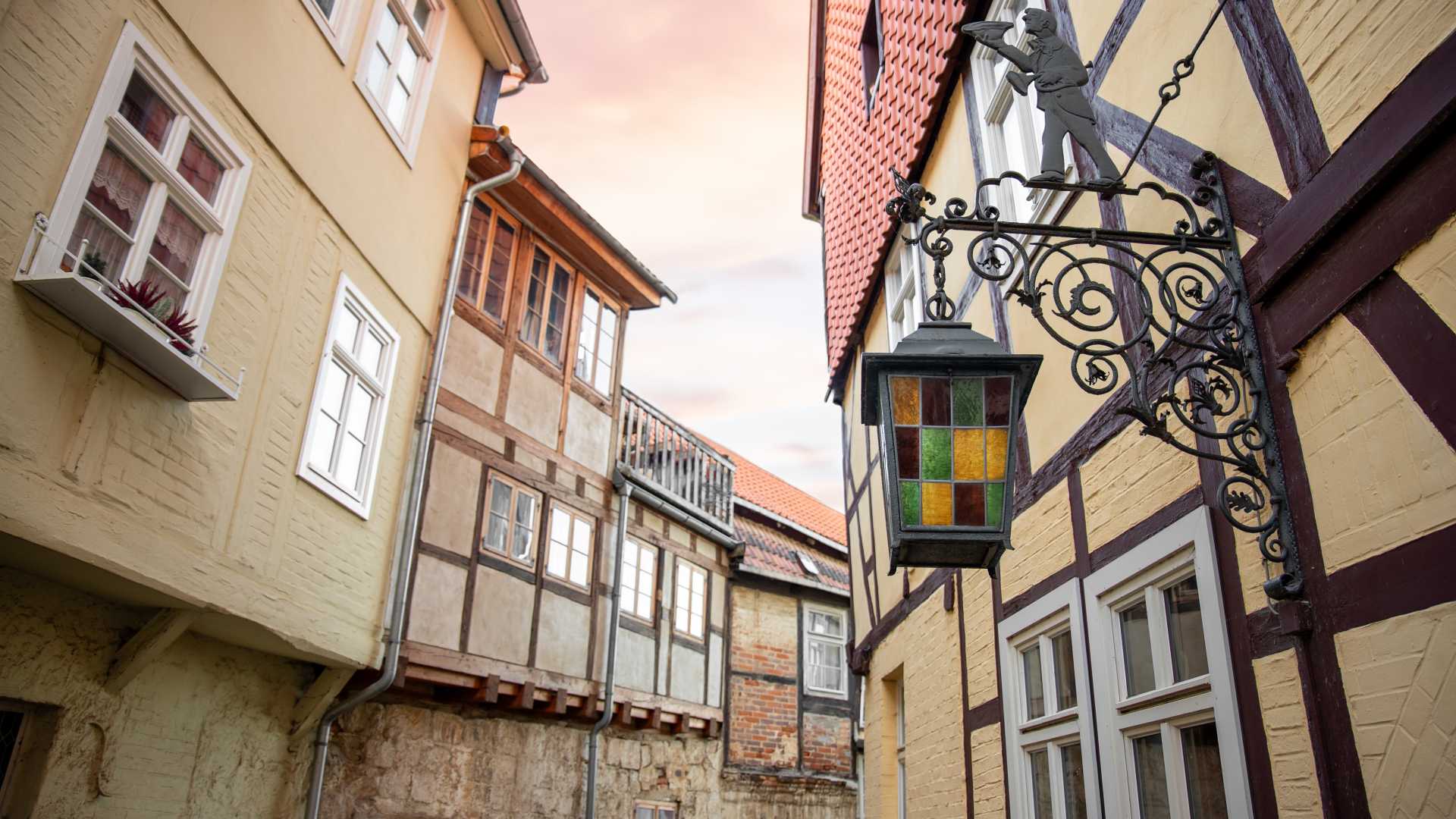 A picturesque street in Wernigerode, Germany, featuring half-timbered houses and a vintage stained glass lantern at dusk.