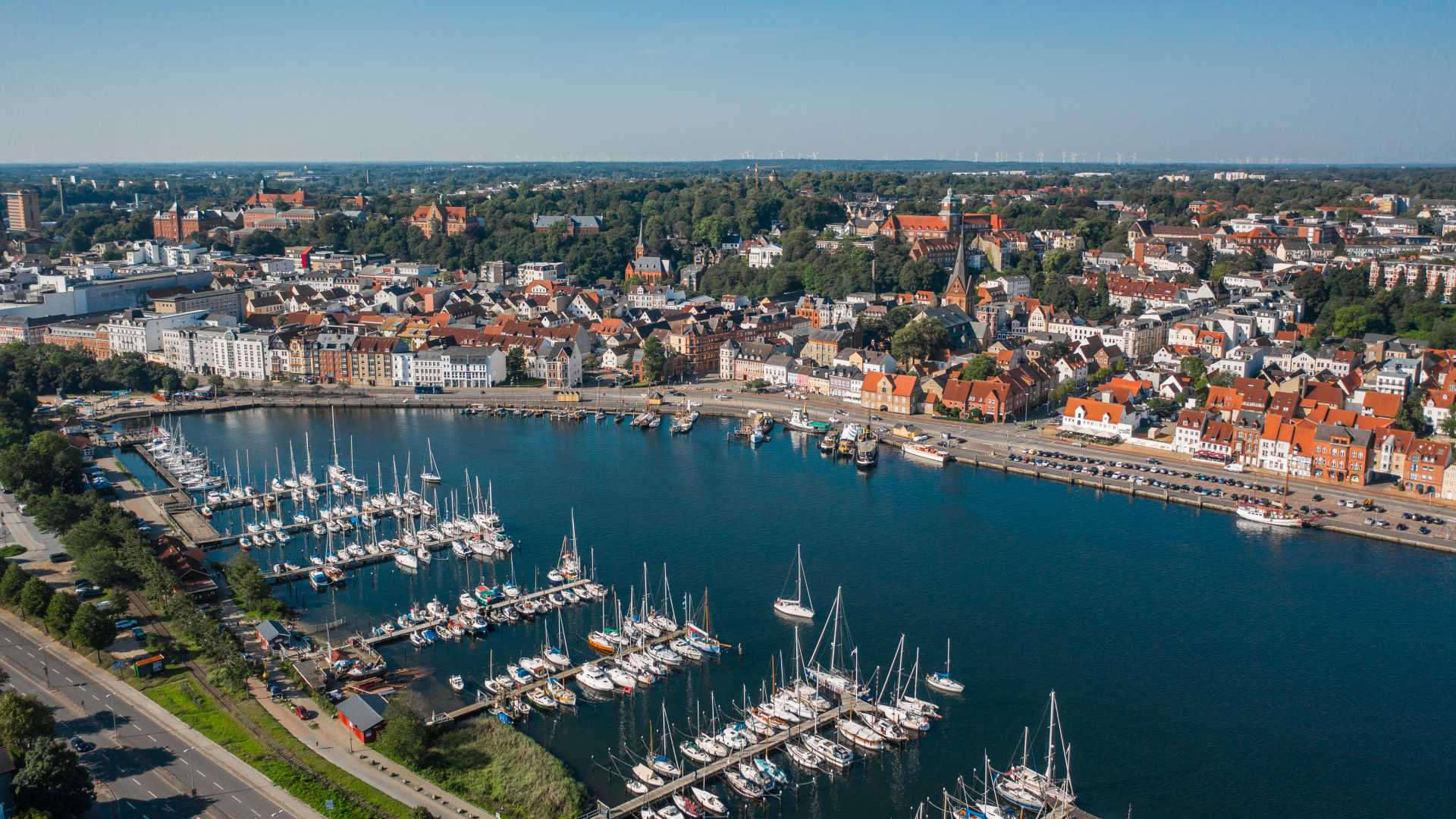 Aerial view of Flensburg's harbor with sailboats, historic buildings, and greenery.