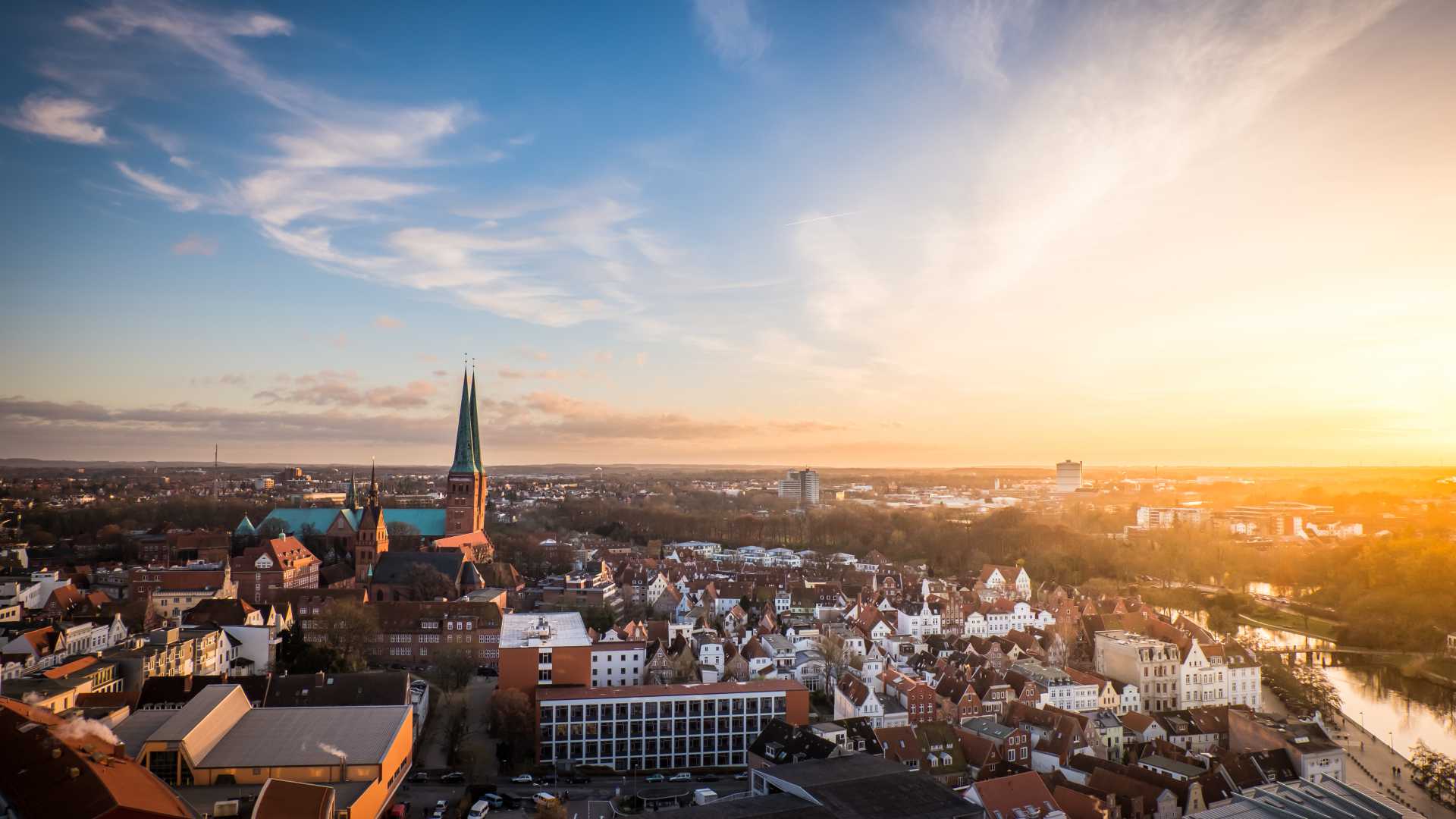 Aerial view of Lübeck at sunset, showcasing historic architecture and church spires under a golden sky.