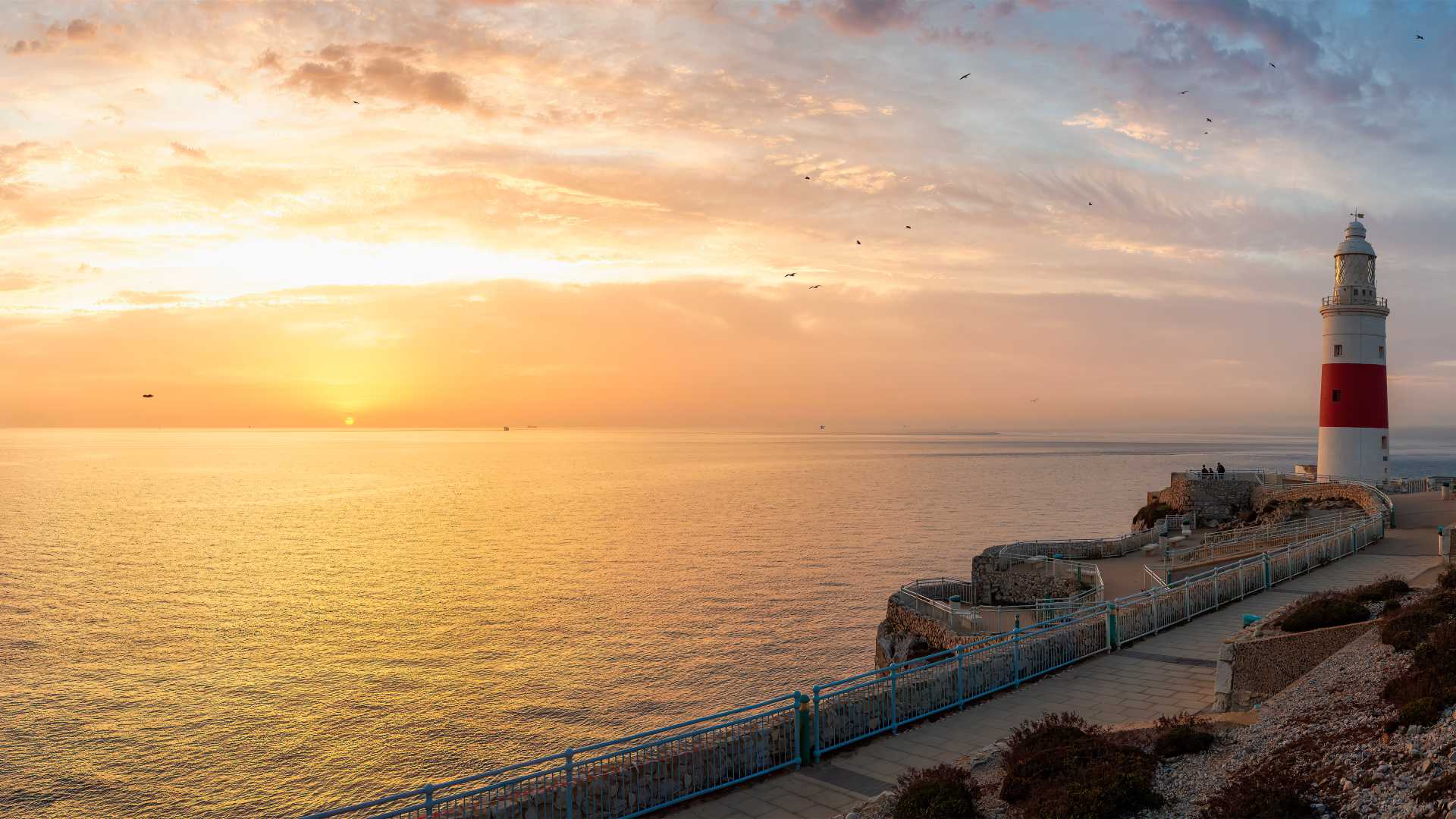 Faro di Europa Point all'alba, Gibilterra, con cieli vibranti e acque tranquille.