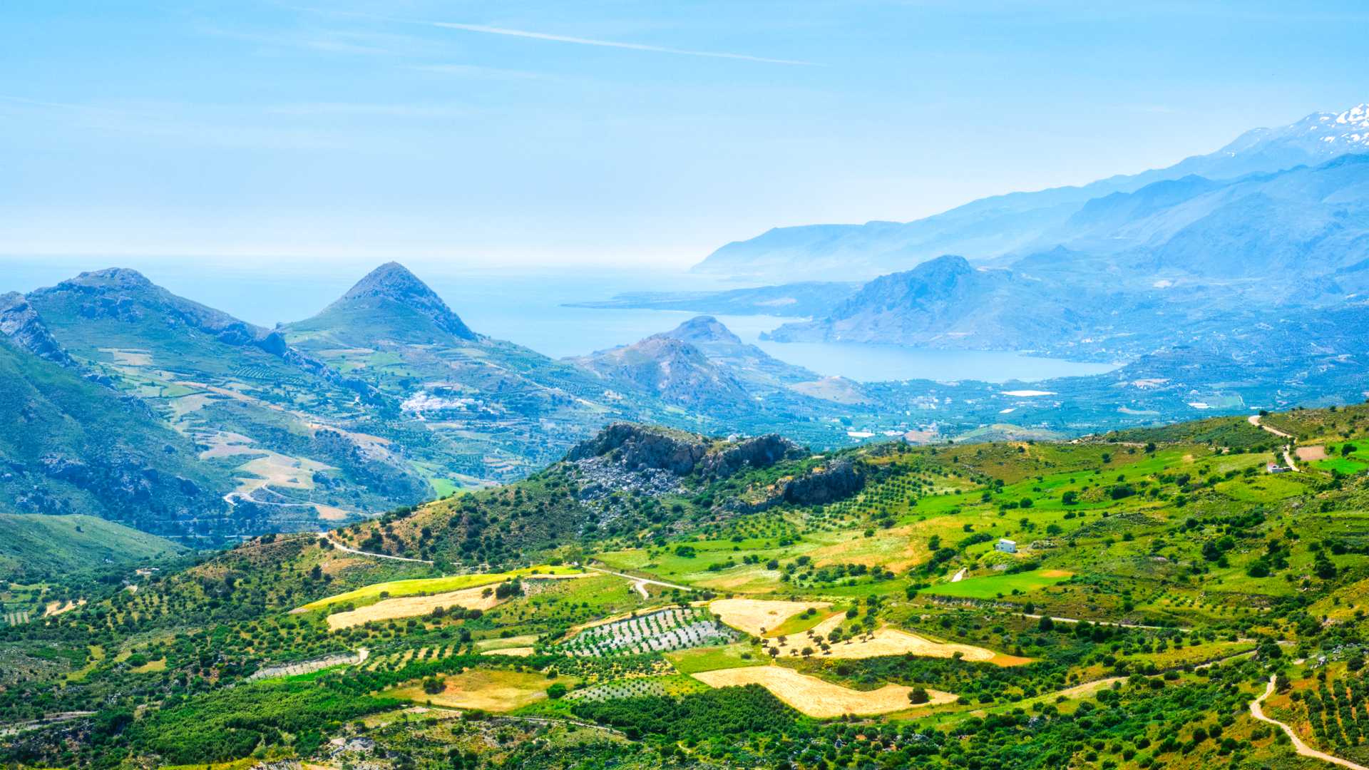 Weelderige velden en bergen ontmoeten de blauwe zee in Kreta onder een heldere hemel.