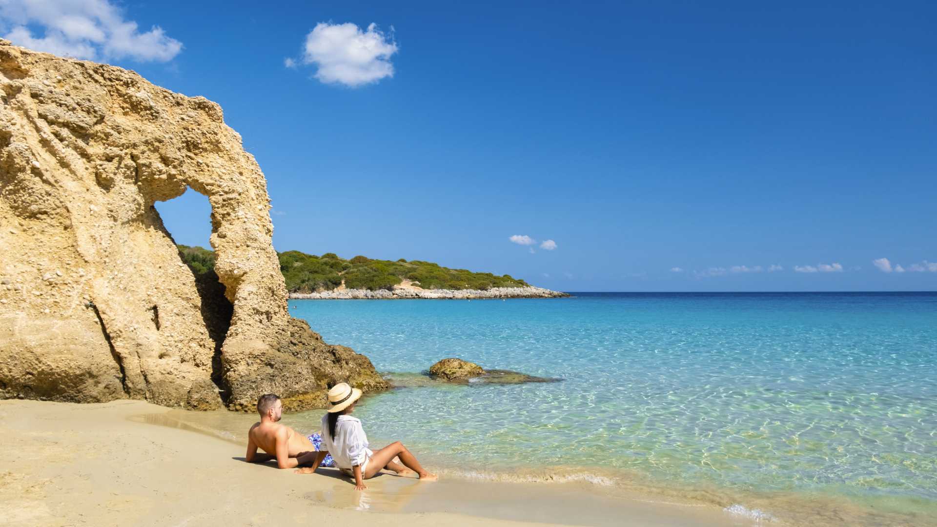Een stel geniet van het kristalheldere water en het gouden zand van Voulisma Beach op Kreta, omgeven door rotsachtige kliffen.