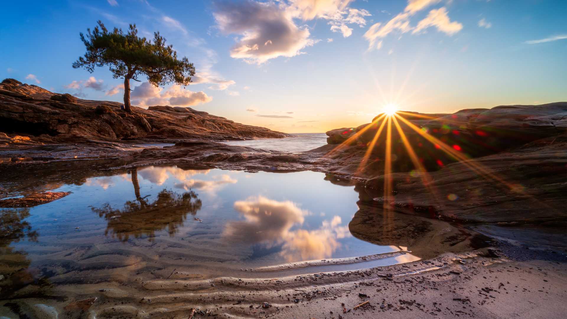 Sunset over Thasos Island's rocky coastline, with sun rays reflecting in a calm tidal pool.