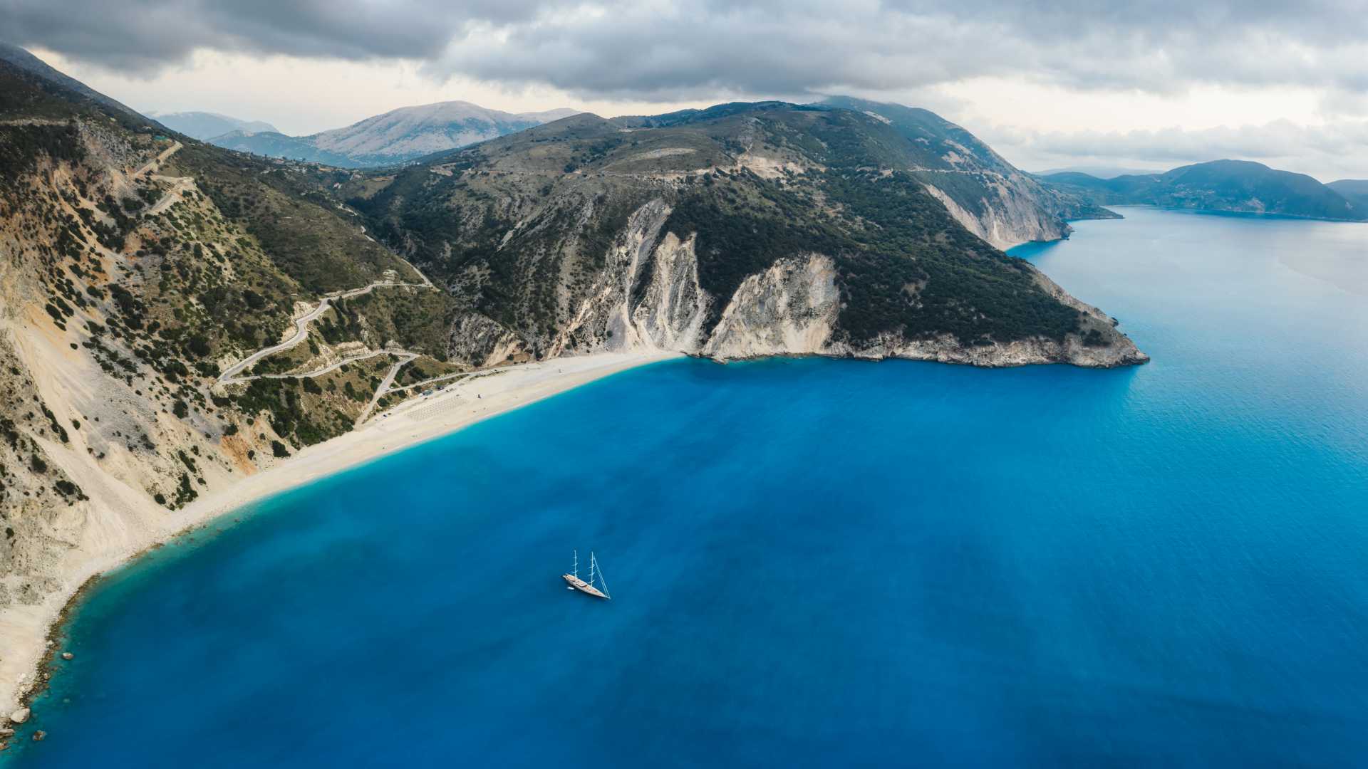 A luxury sail yacht anchored in the turquoise waters of Myrtos Beach, Kefalonia, surrounded by rugged cliffs.