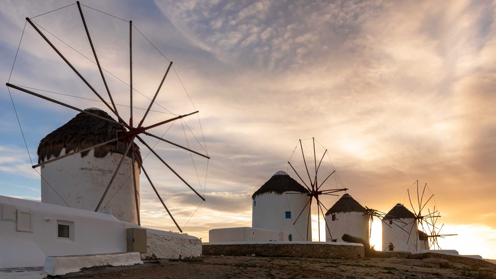 Mykonos windmills silhouetted against a golden sunset, showcasing traditional Cycladic architecture.