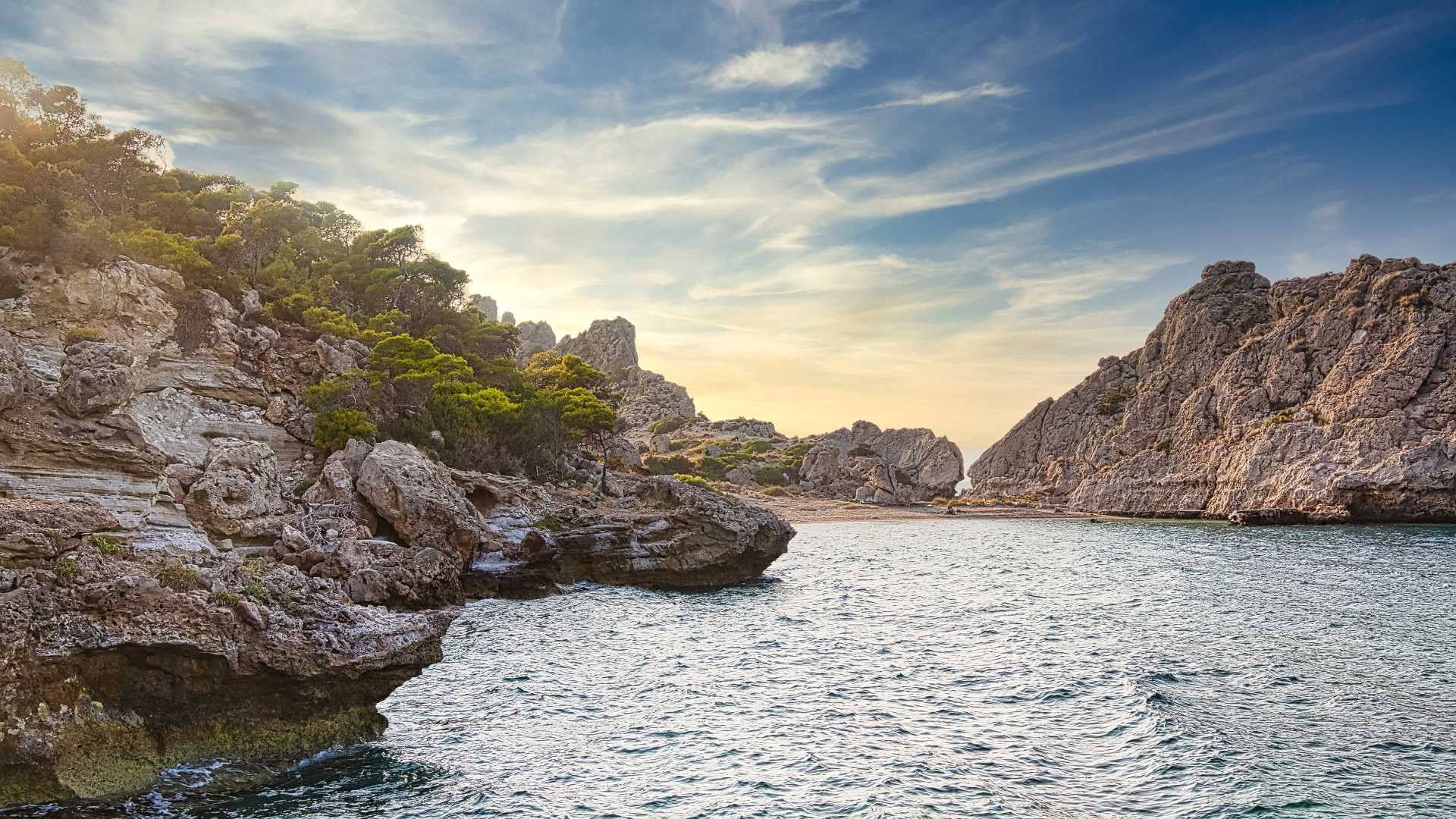 Rotsachtige kliffen en weelderige vegetatie omlijsten het serene water van Sterna Beach onder een levendige lucht in Griekenland.
