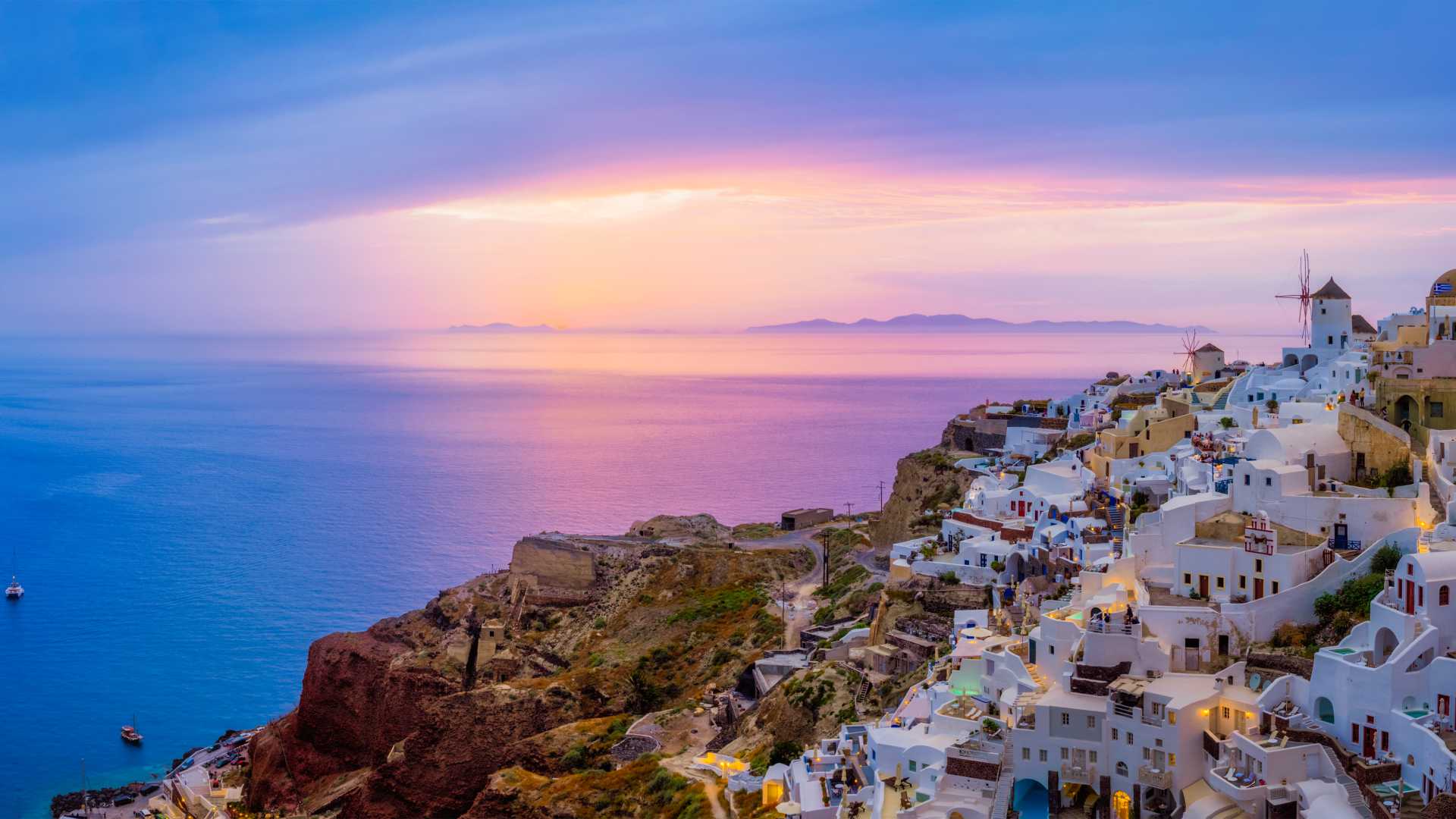 Oia village with white buildings and windmills overlooking the Aegean Sea at sunset in Santorini, Greece.