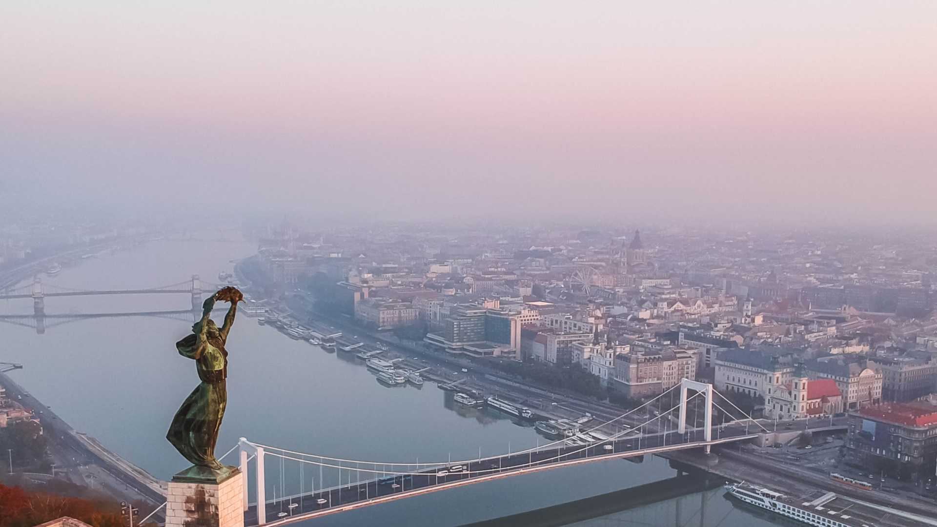 Aerial view of Budapest at sunrise featuring the Statue of Liberty, Elisabeth Bridge, and the Danube.