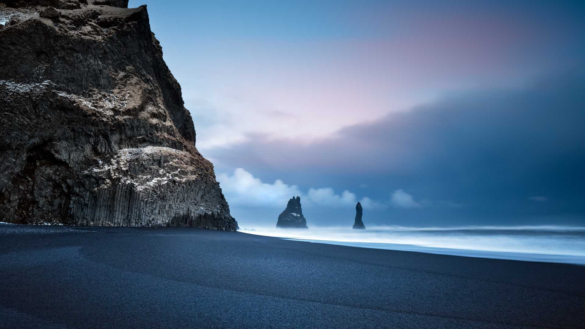 Columnas de basalto y pilas marinas vigilan la playa de arena negra de Reynisfjara, Islandia.