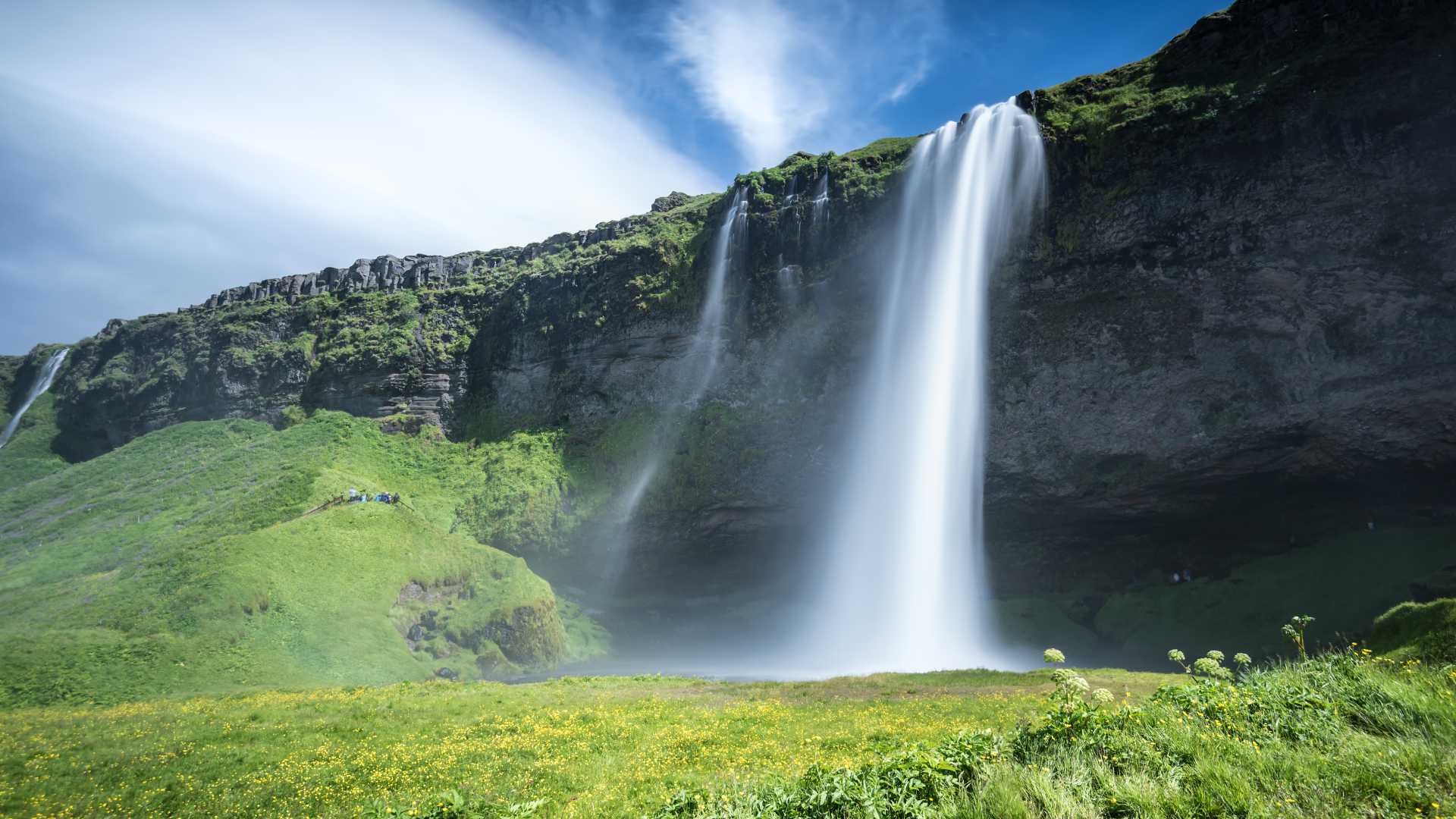 La cascada de Seljalandsfoss desciende con gracia sobre un exuberante acantilado verde bajo el brillante cielo de verano de Islandia.
